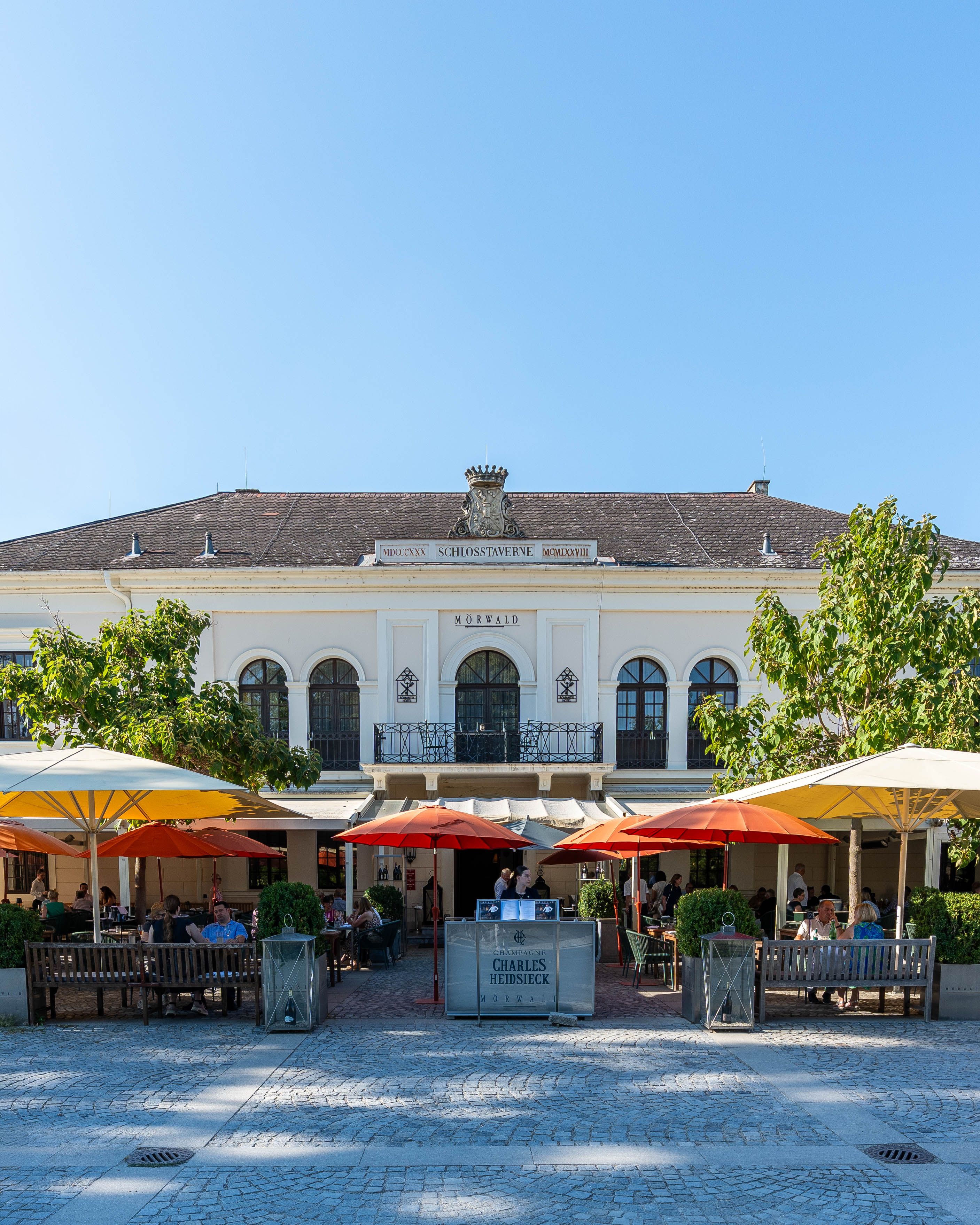A Grafenegg Hotel & Restaurant elölnézete terasszal, napernyőkkel és vendégekkel a Mörwald épület előtt, Grafeneggben.