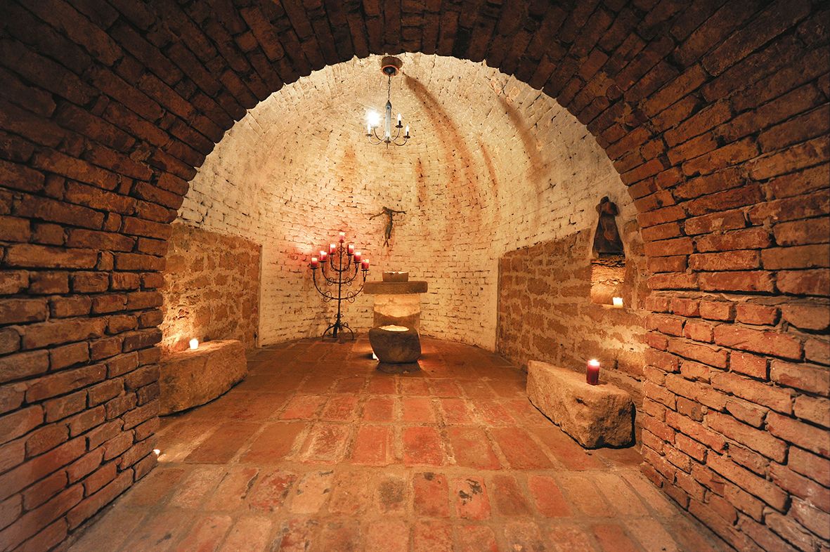 Egy rusztikus, boltíves pincehelyiség gyertyákkal és oltárral.