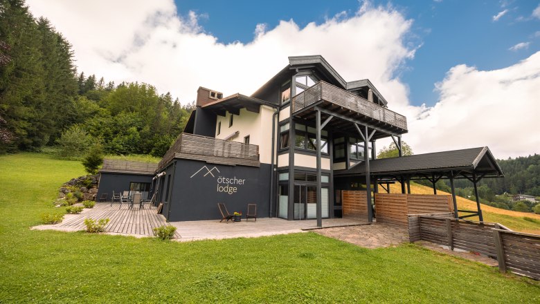 Ötscher Lodge zöld, erdős környezetben, kék égbolt mellett.