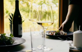 Terített asztal egy üveg borral, borospoharakkal és egy tányér étellel egy étteremben.