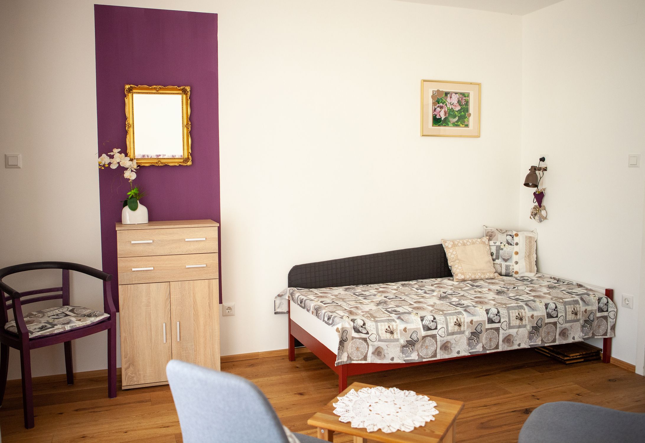 Egy nappali egy kanapéval, egy kis szekrénnyel, egy székkel és egy asztallal a fapadlón.