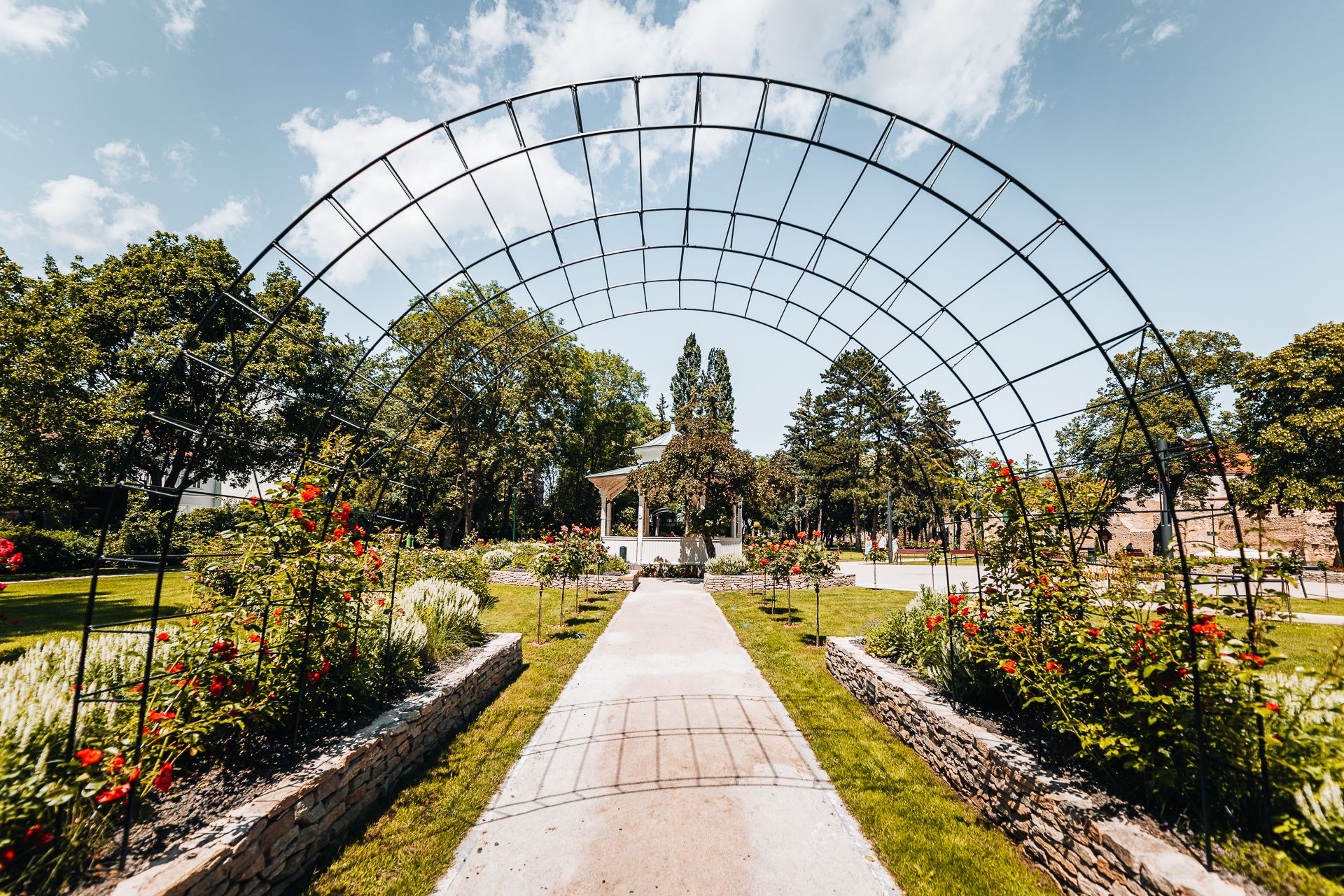 Zöld városi park romantikus pavilonnal, rózsakerttel és rácsos boltívvel