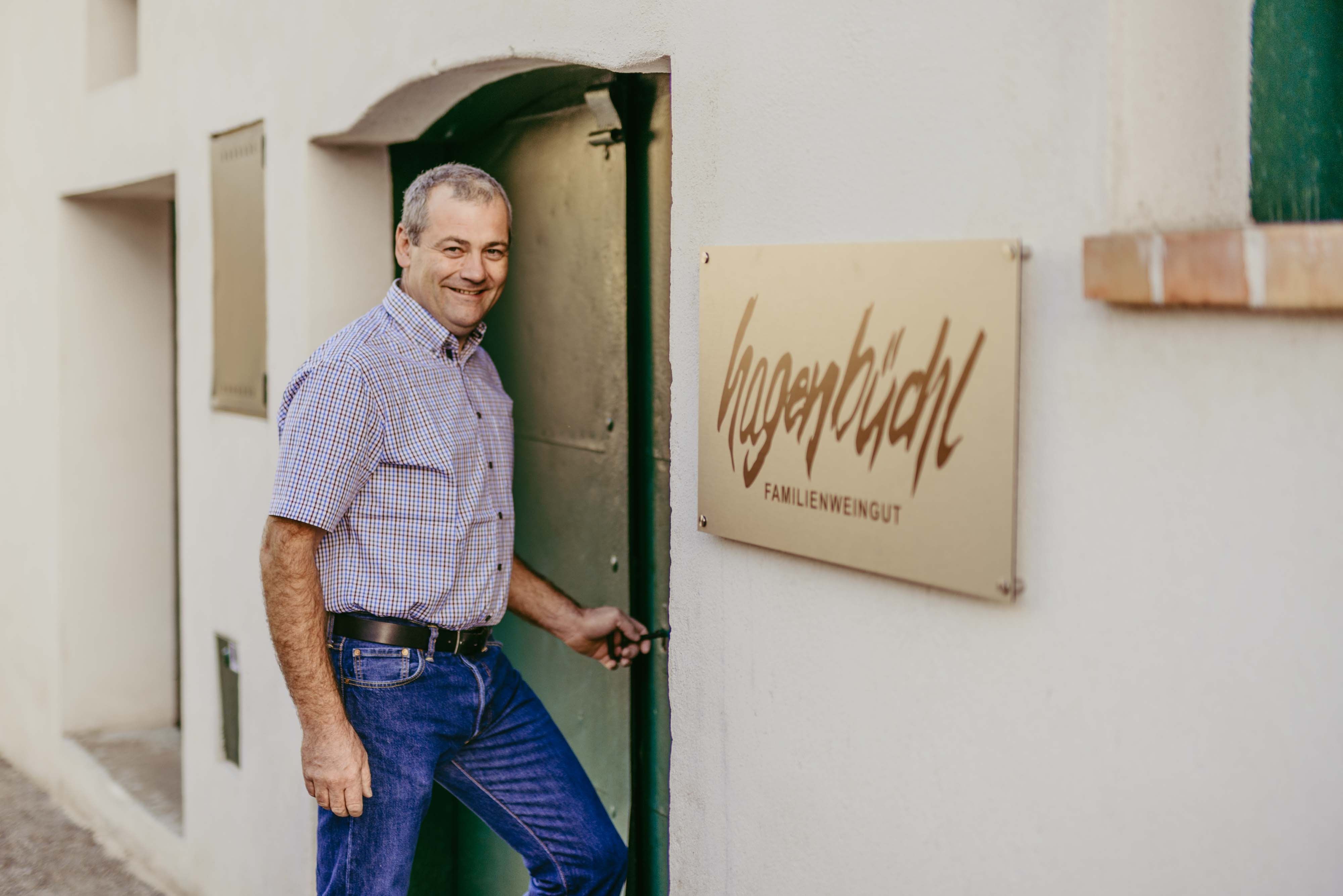 Egy férfi kinyit egy ajtót egy tábla mellett, amelyen az áll: "Hagenbüchl Familienweingut".