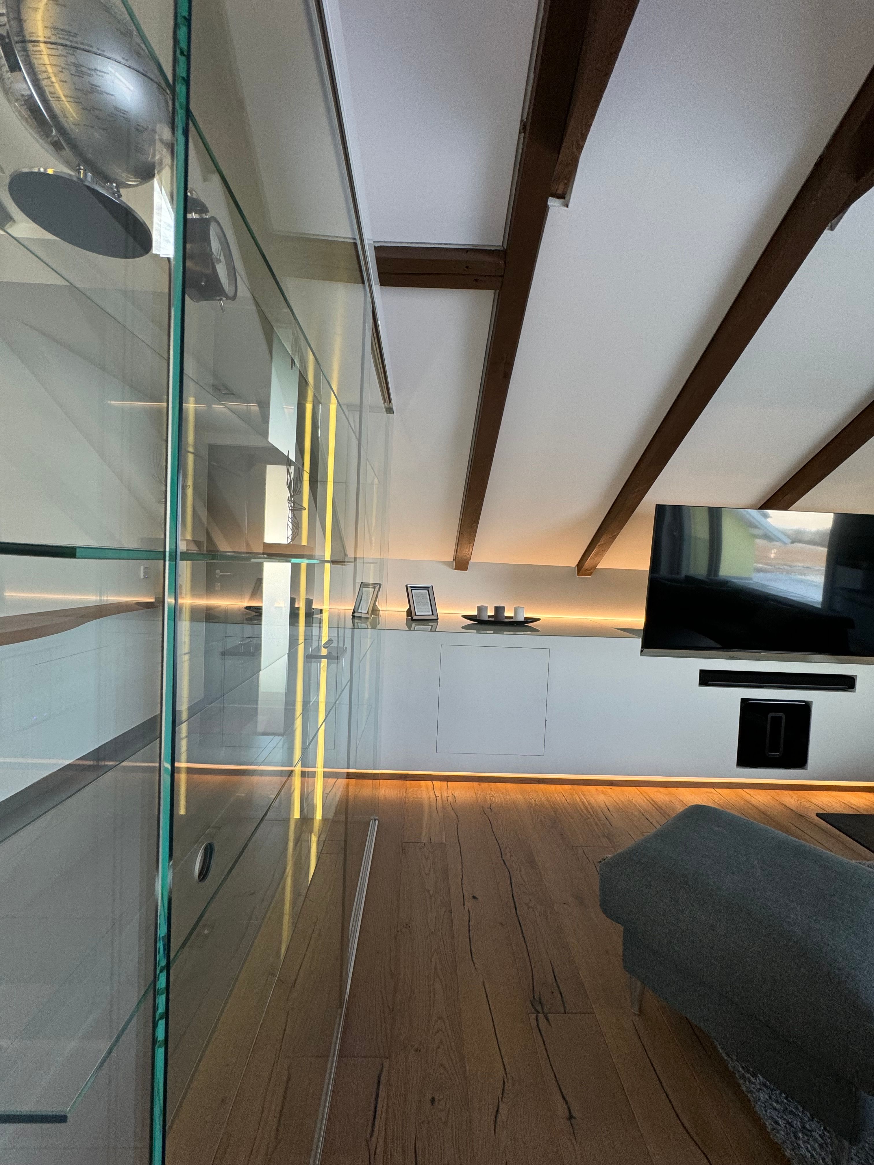 Modern nappali fapadlóval, üvegszekrénnyel, TV-vel és ferde mennyezetű fagerendákkal.