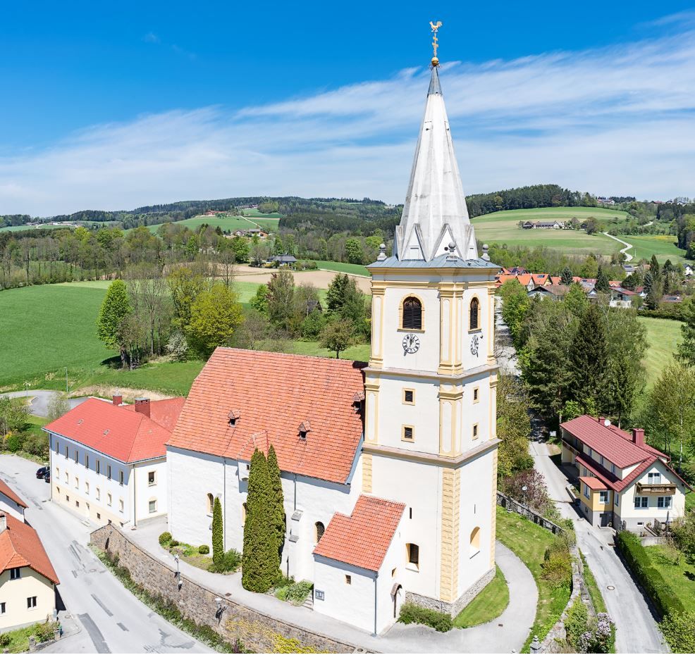 Légi felvétel Krumbach erődtemplomáról vidéki környezetben, zöld mezőkkel és kék éggel.