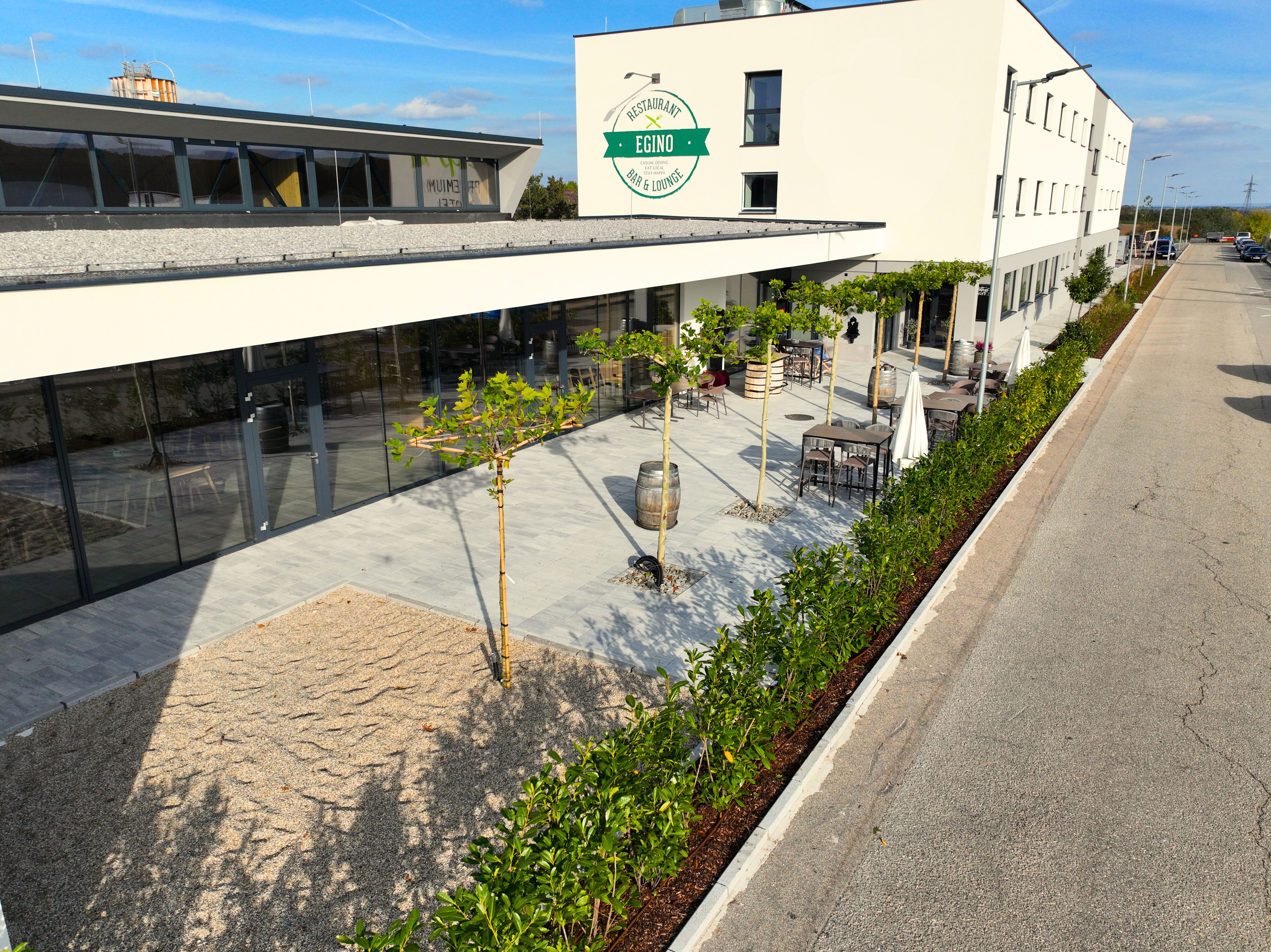 Egy modern épület külső nézete terasszal és növényekkel.