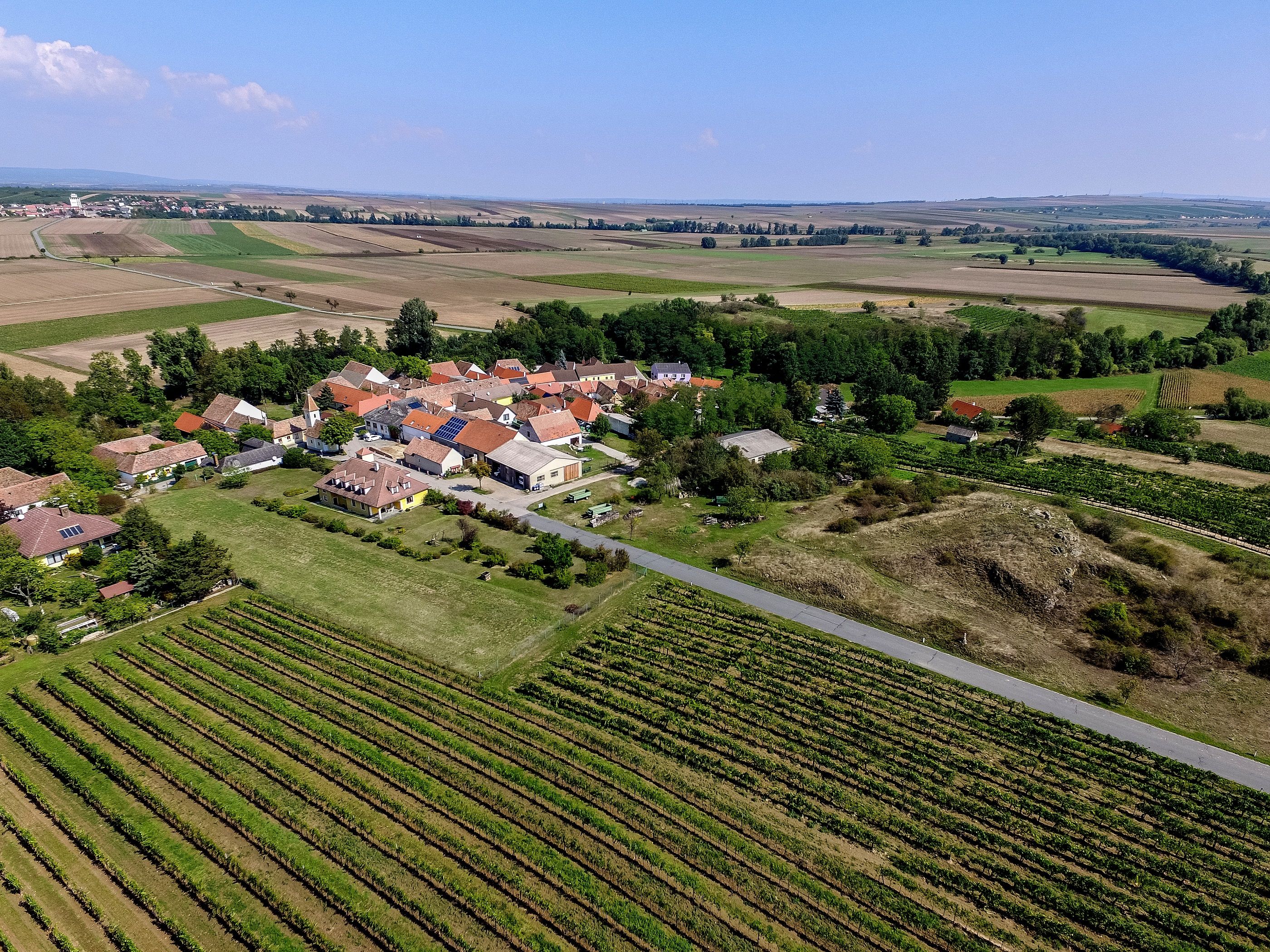 Légi felvétel egy kis faluról, amelyet mezők és szőlőültetvények vesznek körül.