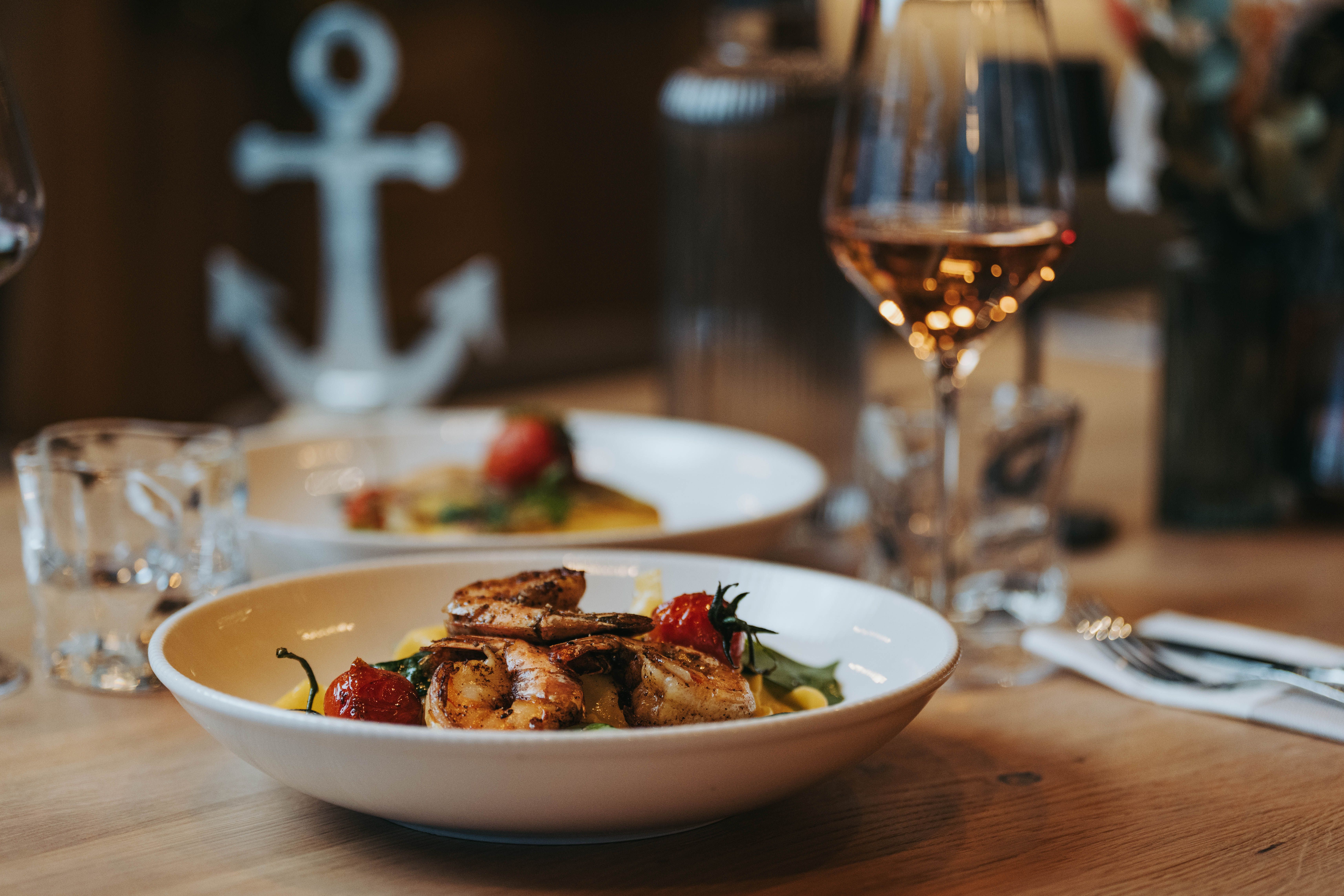 Egy tányér garnélarák és zöldségek az asztalon, mellette egy pohár bor.