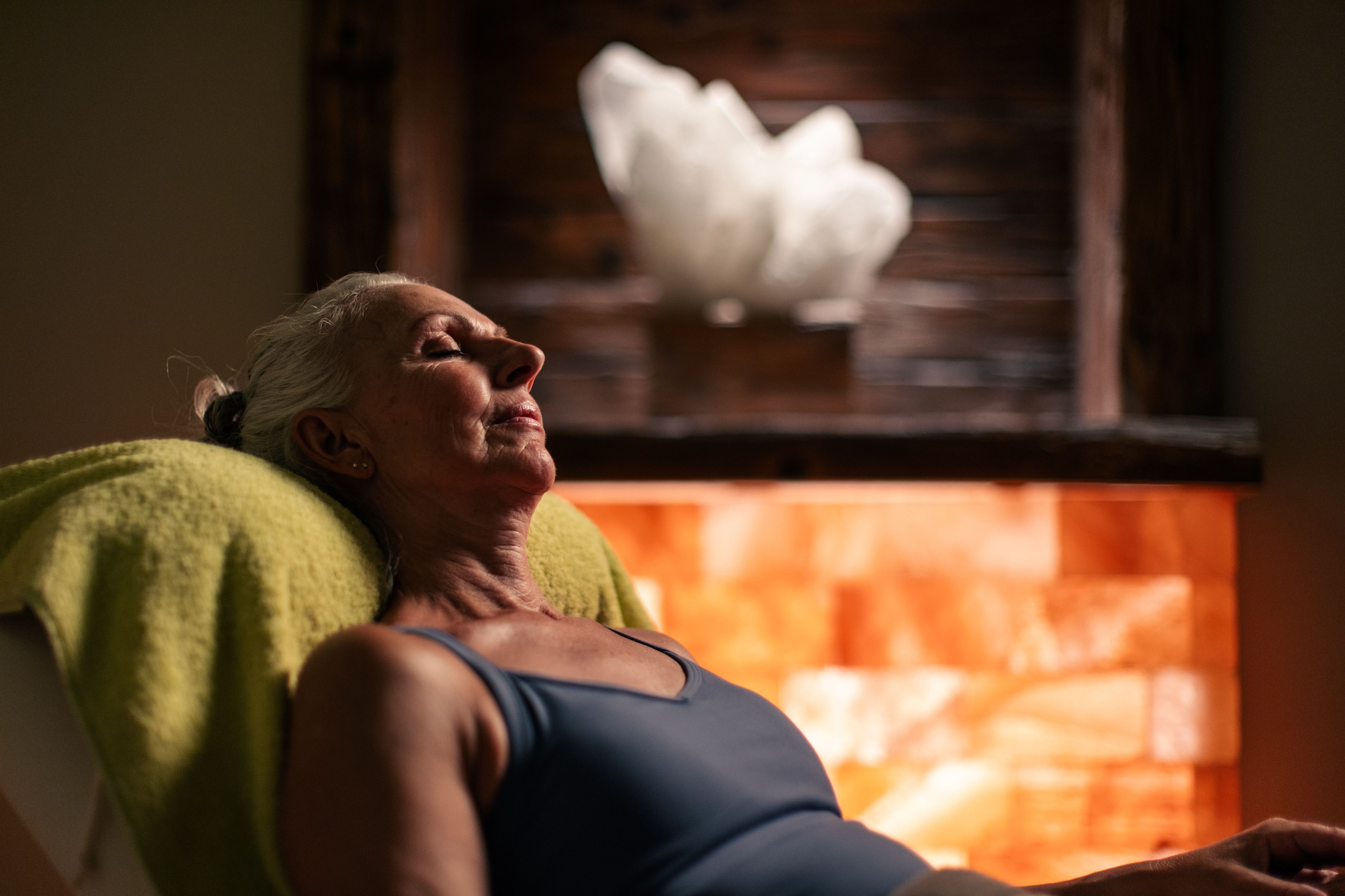 Egy idős hölgy pihen egy wellnessközpontban, meleg fény és sókő háttér közepette.