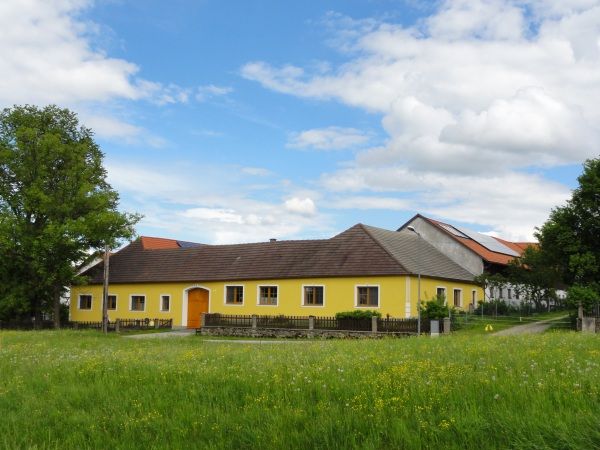 Sárga parasztház zöld réten, kék éggel és felhőkkel.