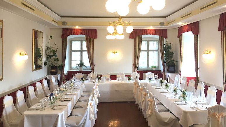 Elegáns terem a Gloggnitz-kastélyban, díszített banketthez, fehér terítőkkel és székekkel.
