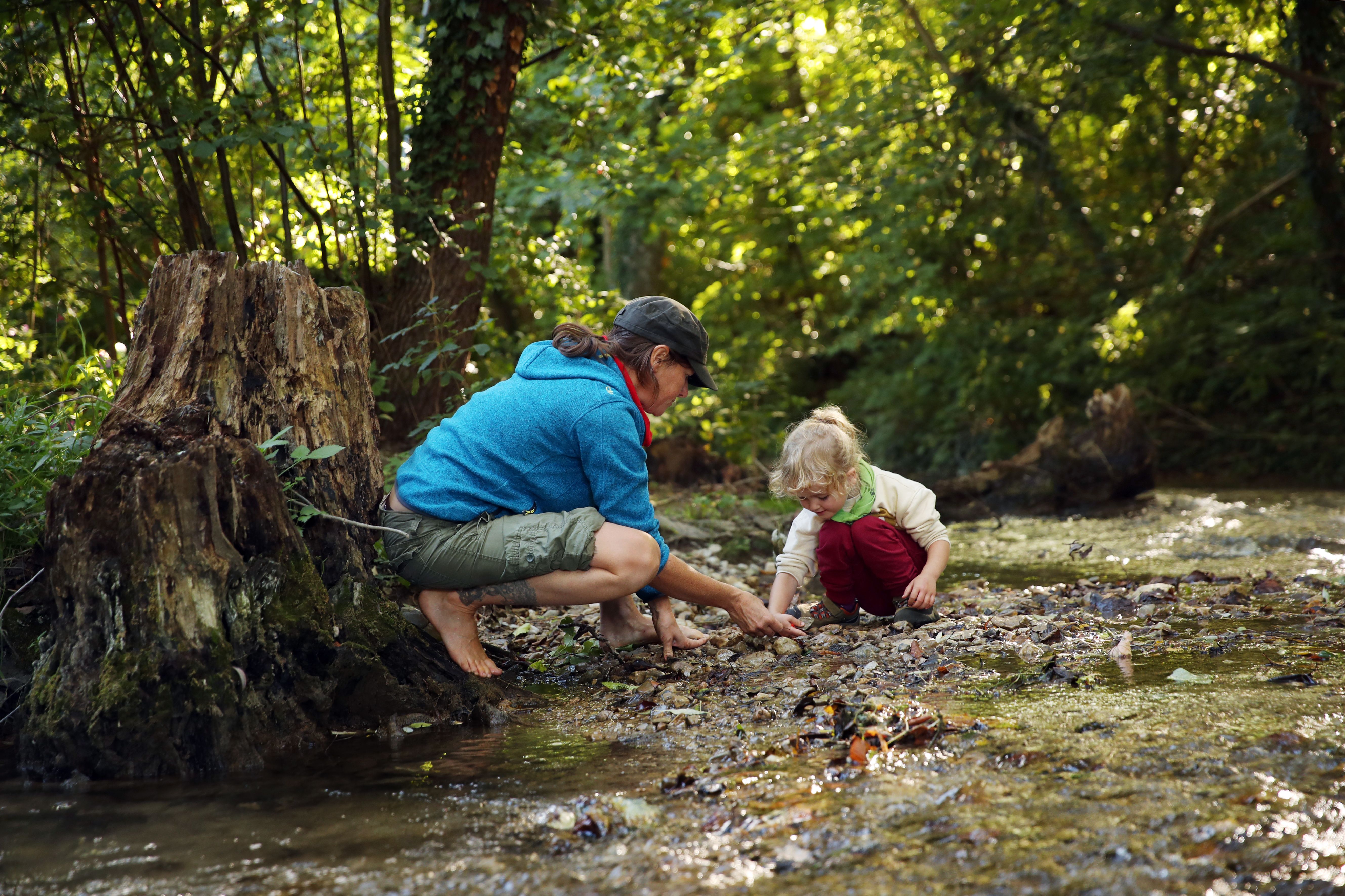 Egy felnőtt és egy gyermek egy erdei patak mellett játszik.
