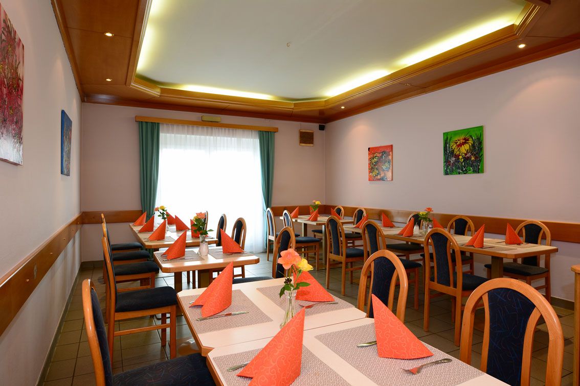 Egy étkező terített asztalokkal, narancssárga szalvétákkal és virágvázákkal.