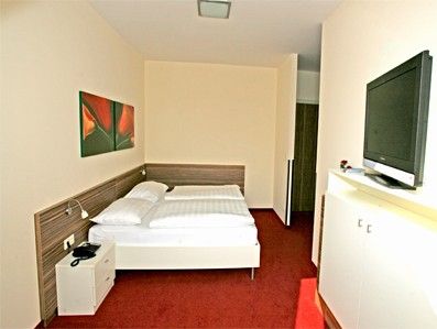 Hotelszoba franciaággyal, vörös szőnyeggel és freskóval.