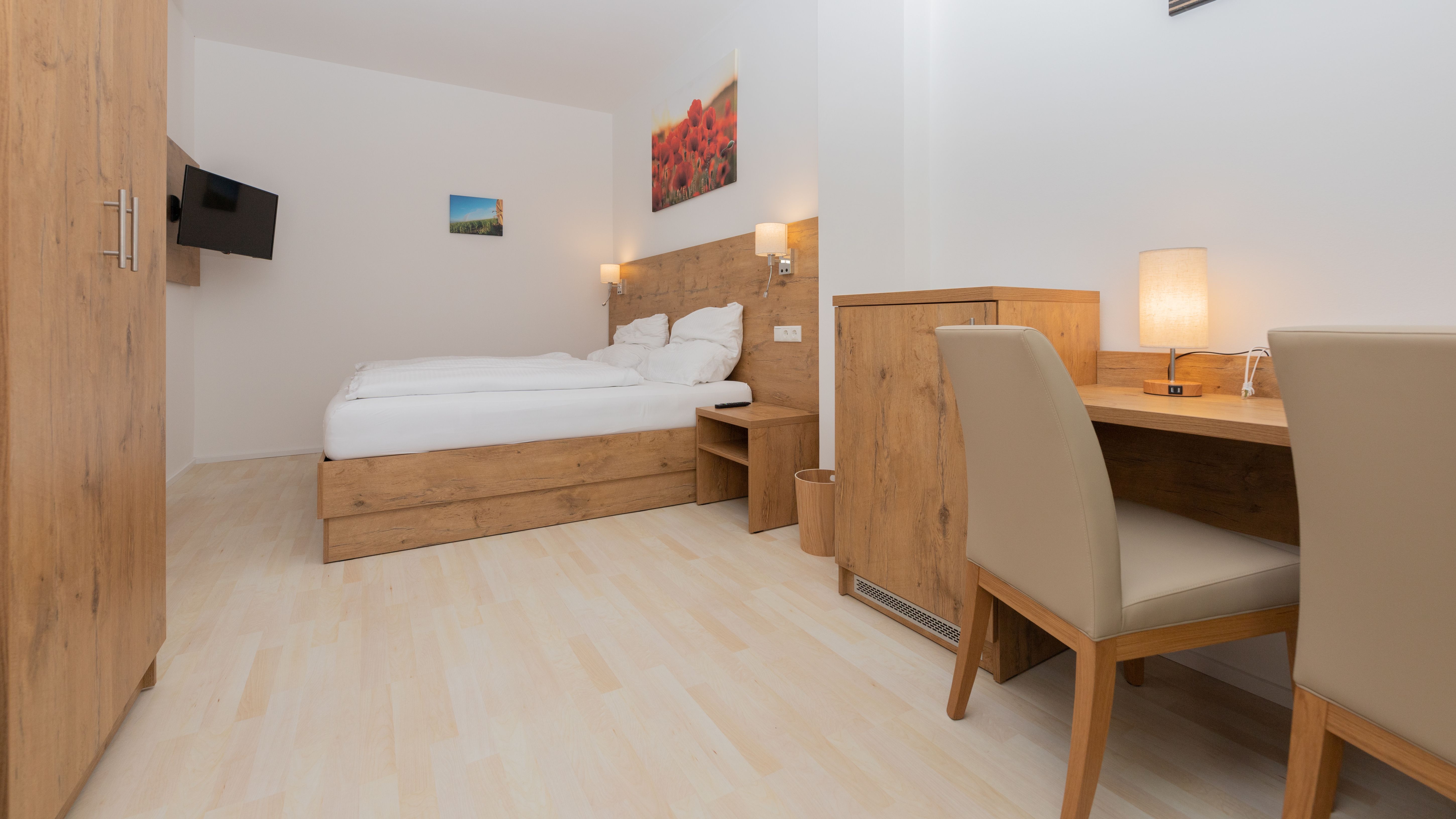 Modern hálószoba fabútorokkal, franciaággyal, íróasztallal és síkképernyős TV-vel.