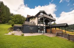 Ötscher Lodge zöld, erdős környezetben, kék égbolt mellett.