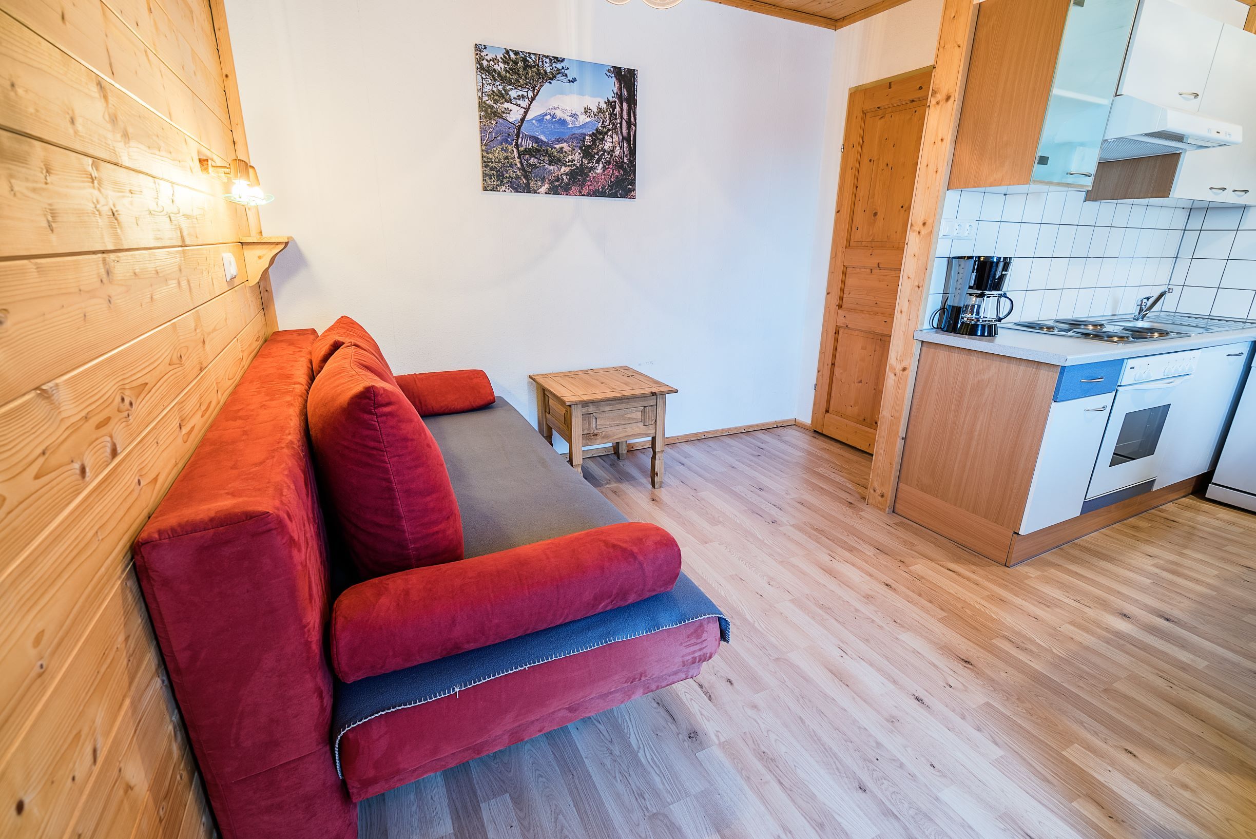 Nappali piros kanapéval, fából készült falakkal és kis konyhával.