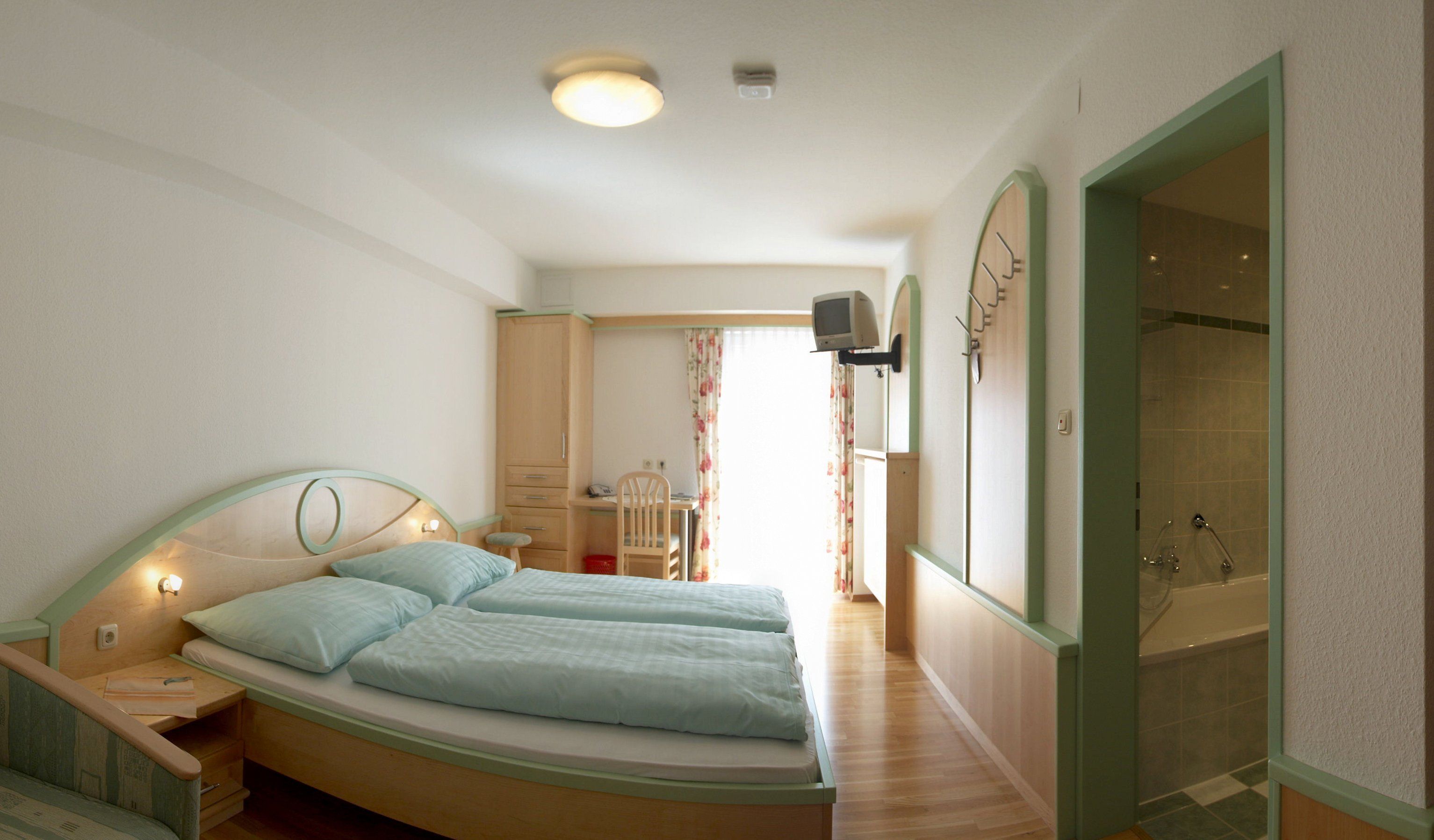 Hotelszoba franciaággyal, íróasztallal, televízióval és fürdőszobával.
