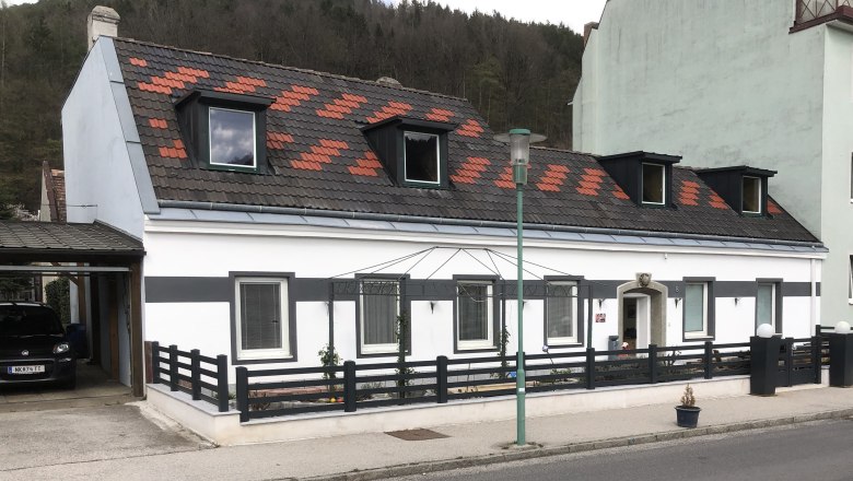 Egy feh&eacute;r h&aacute;z l&aacute;tk&eacute;pe fekete ker&iacute;t&eacute;ssel &eacute;s tetőablakokkal.