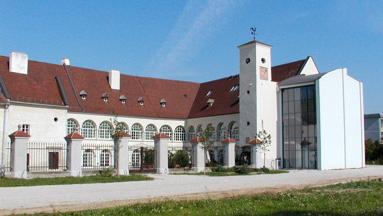 Katzelsdorf kastély modern bővítéssel és történelmi épülettel. Fehér homlokzat kerek ablakokkal, piros tetővel és nagy belső udvarral.