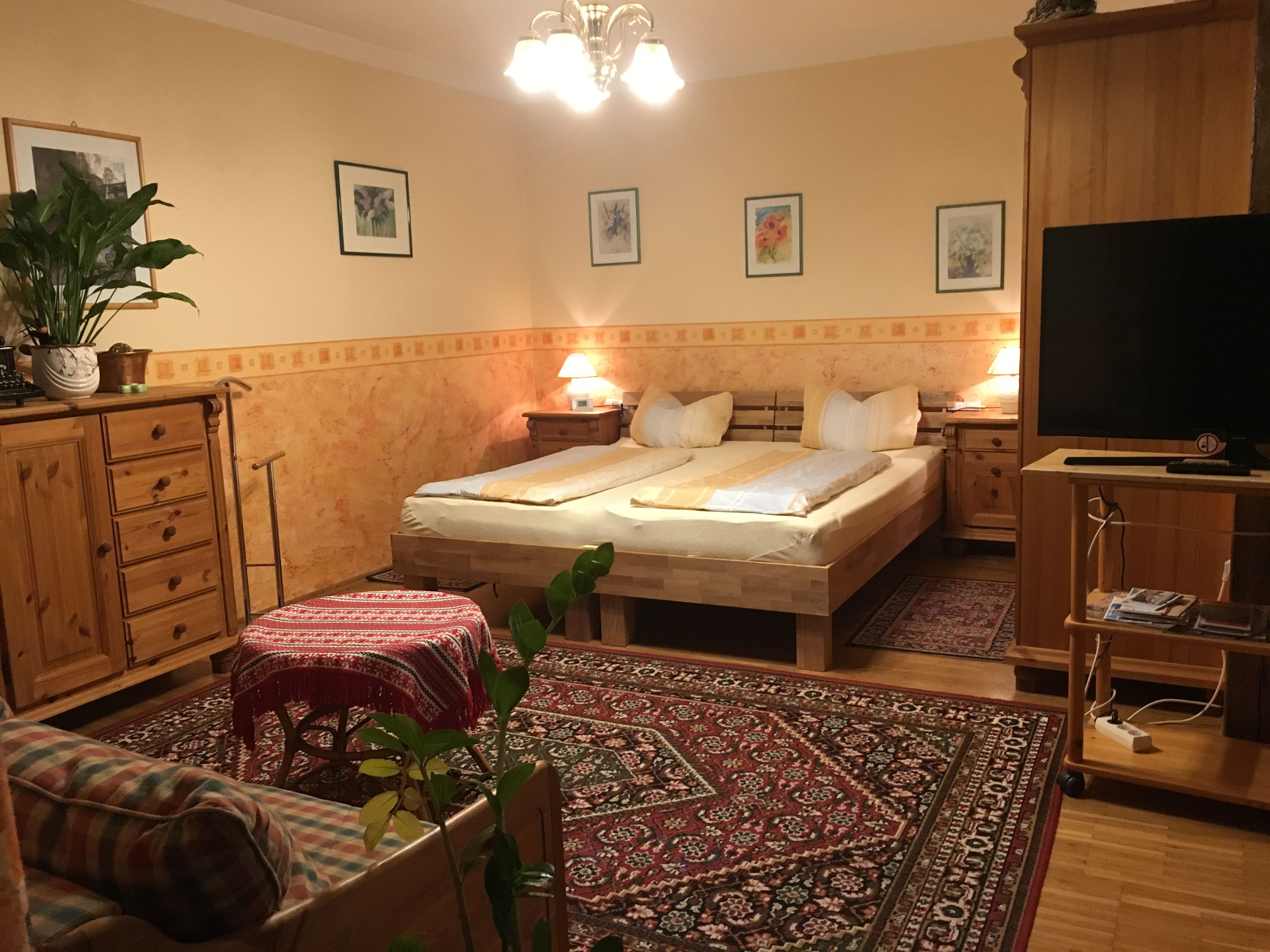 Hangulatos hálószoba fabútorokkal, franciaággyal, szőnyeggel és növényekkel.