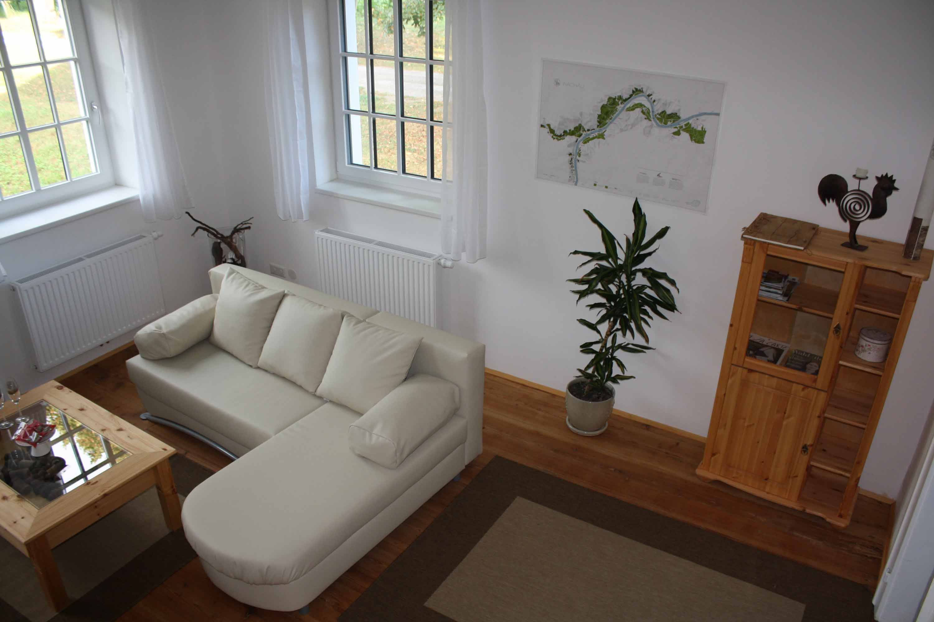 Hangulatos nappali bézs színű kanapéval, fa asztallal, növényekkel és polccal egy nyaraló apartmanban.