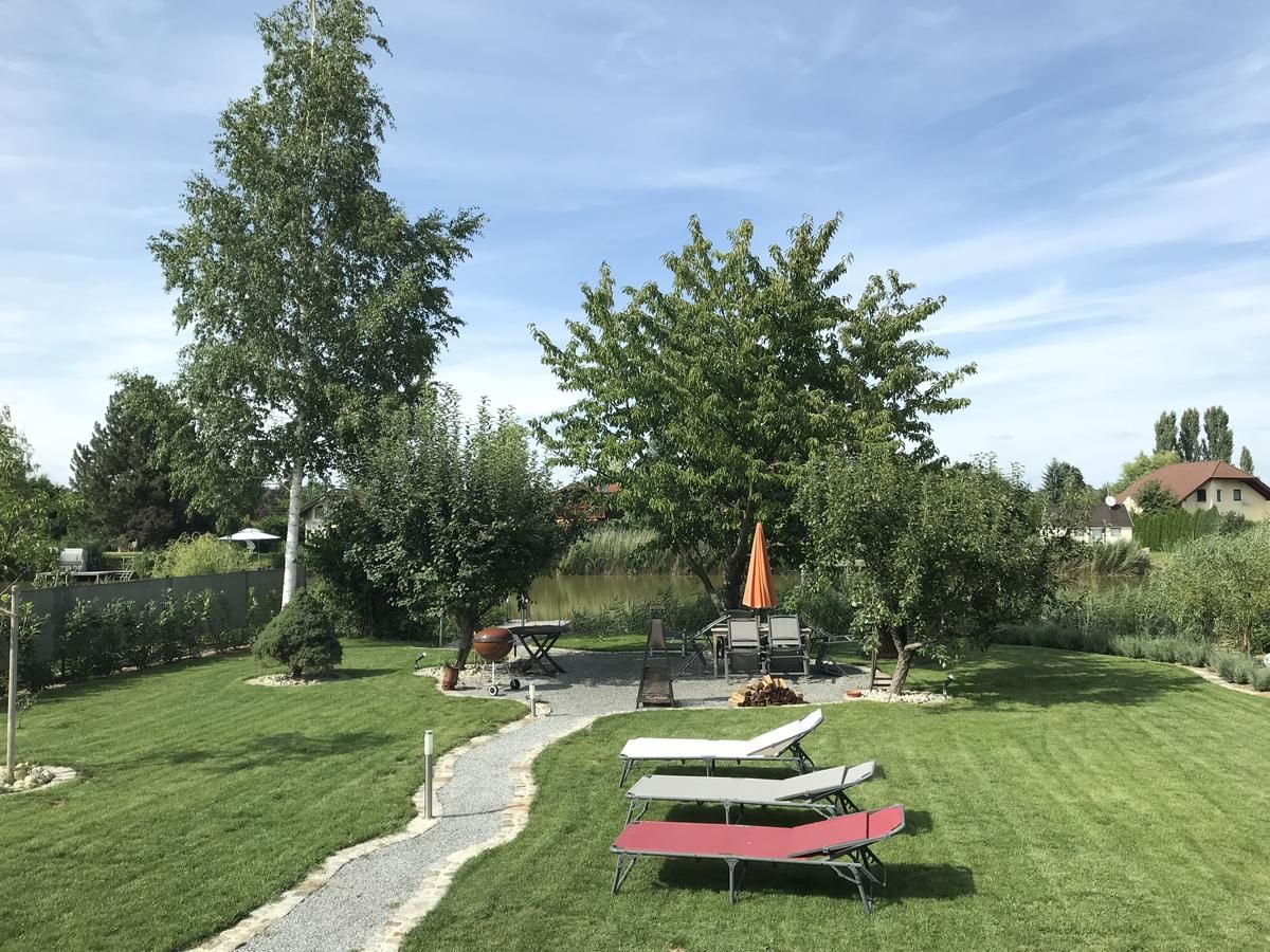 A gondozott kertben pázsit, fák, napozóágyak és egy asztal napernyővel.