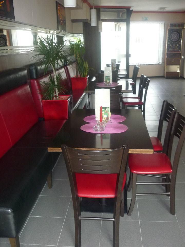 Egy kávézó belső nézete, piros és fekete bútorokkal, növényekkel és egy darts-géppel.