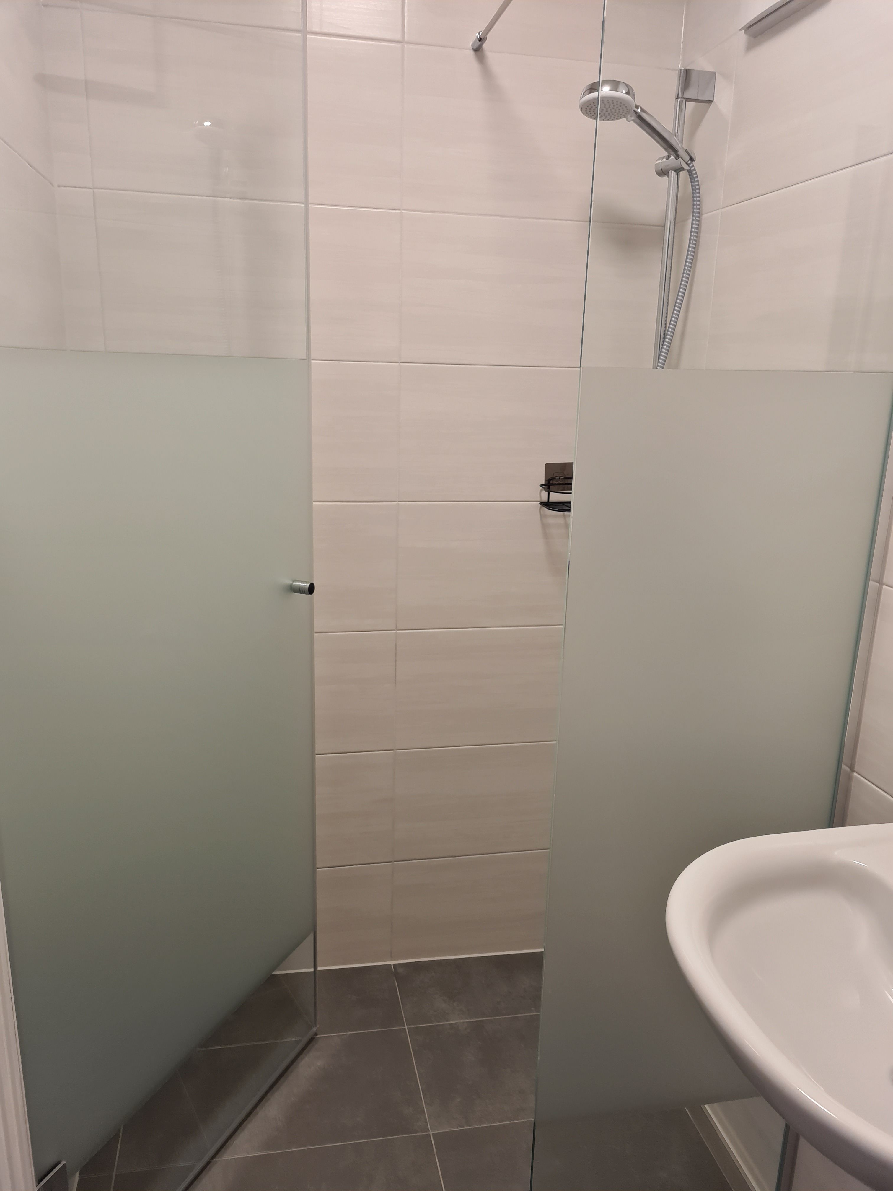 Modern zuhanyzó üvegfalakkal és zuhanyfejjel egy fürdőszobában.