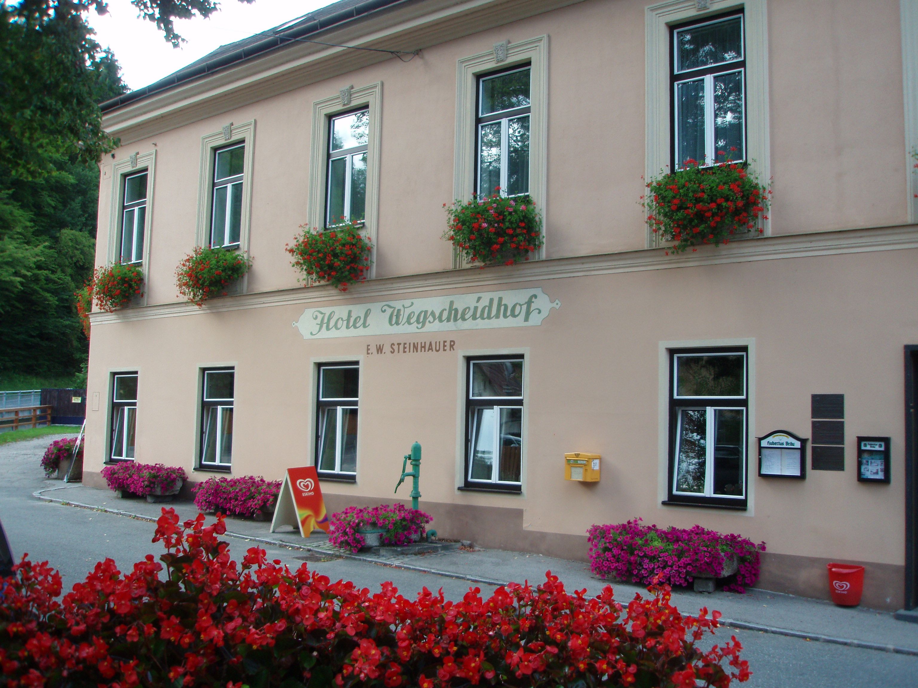 A Hotel Wegscheidhof homlokzata virágládákkal és táblákkal.