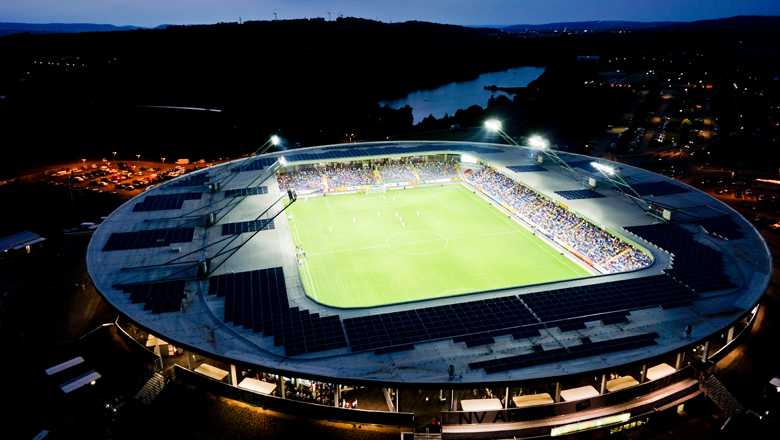 Egy kivilágított labdarúgó-stadion légi felvétele éjszaka.