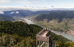 Von der Aussichtsplattform eröffnet sich ein atemberaubender Blick über die sanften Hügel und die glitzernde Donau, die sich durch die malerische Landschaft schlängelt. Die frische Bergluft und das sanfte Rauschen der Bäume laden dazu ein, einen Moment innezuhalten und die Schönheit der Natur zu genießen.
