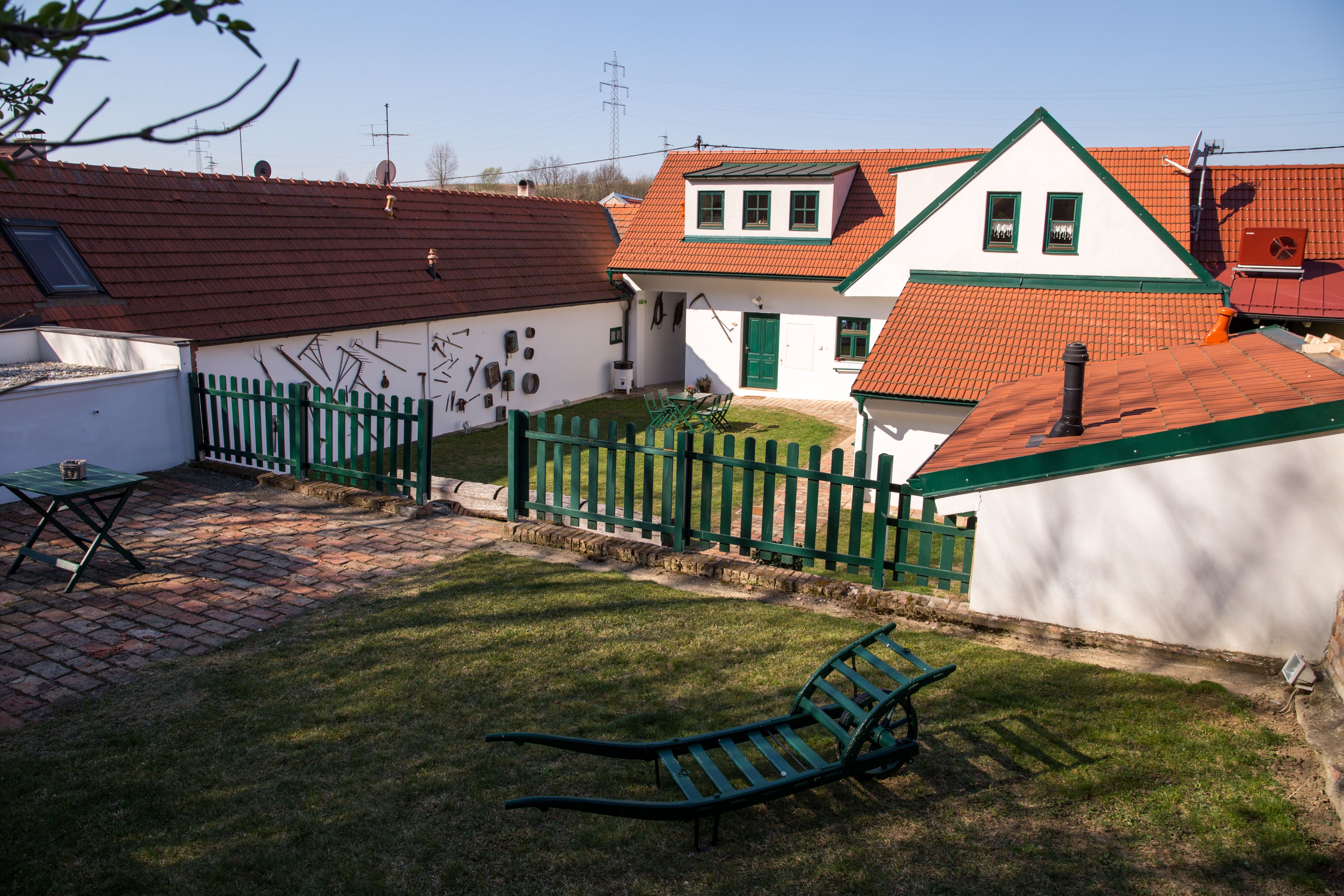 Hagyományos szőlőskert piros cseréptetőkkel, zöld kerítéssel és kerti bútorokkal egy réten.