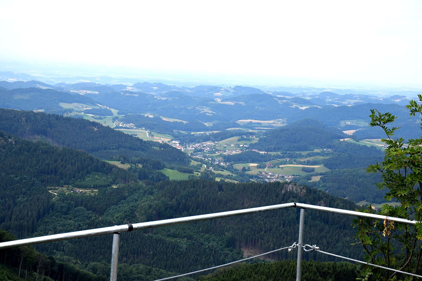 Kilátás a vár kőfaláról egy dombos tájra, erdőkkel és falvakkal.