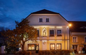 Szent Flórián fogadó alkonyatkor, kivilágított homlokzattal és szoborral.