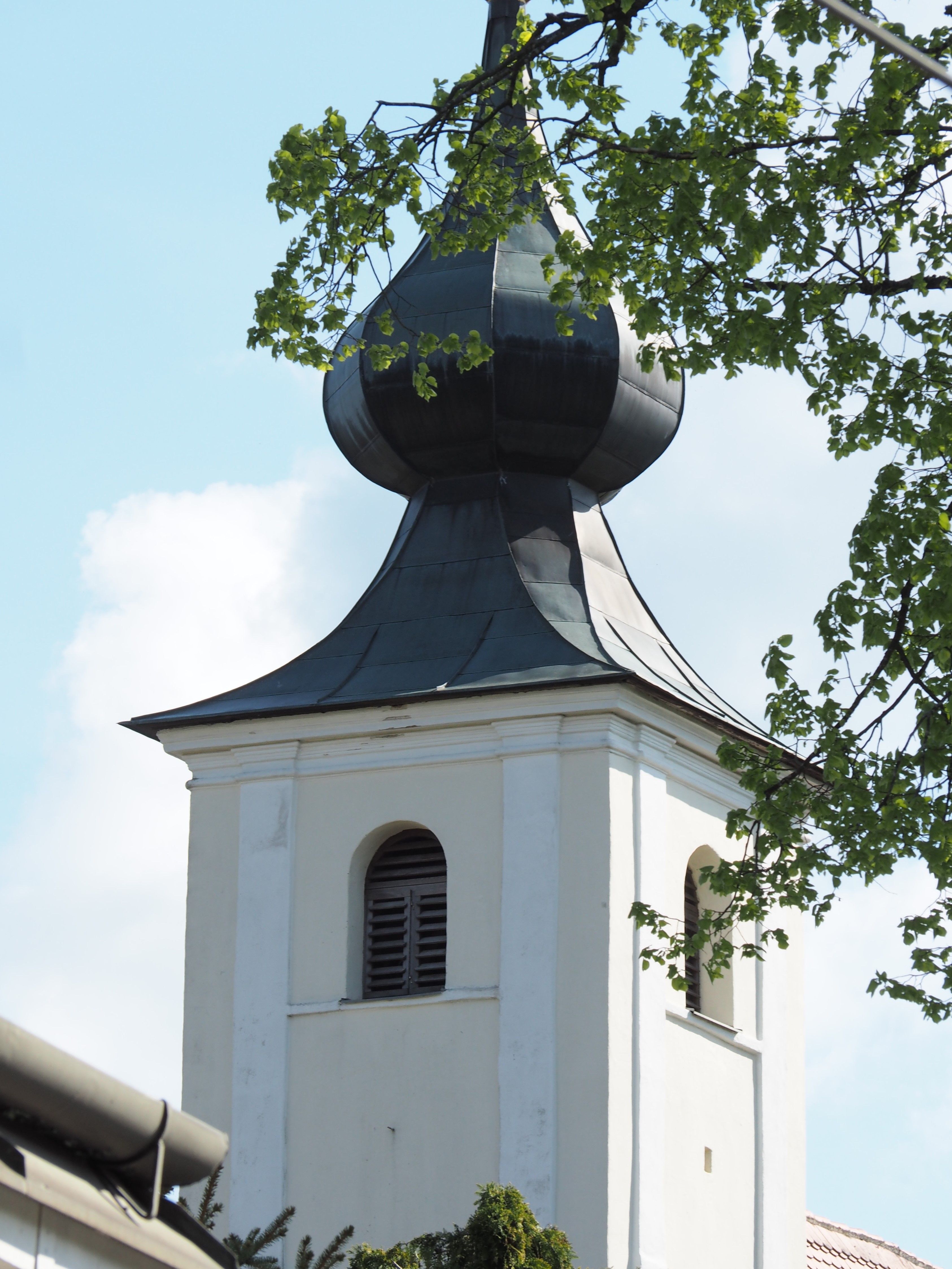 Templomtorony hagymakupolával és zöld levelekkel az előtérben.