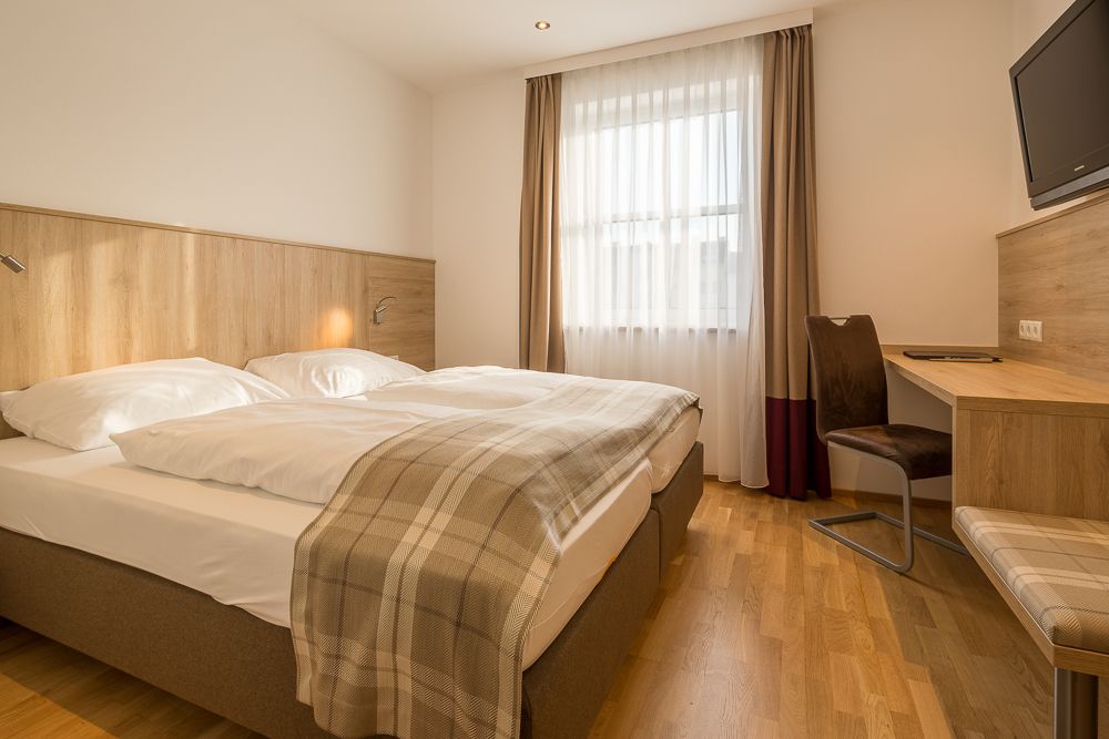 Hotelszoba franciaággyal, íróasztallal és függönyös ablakkal.