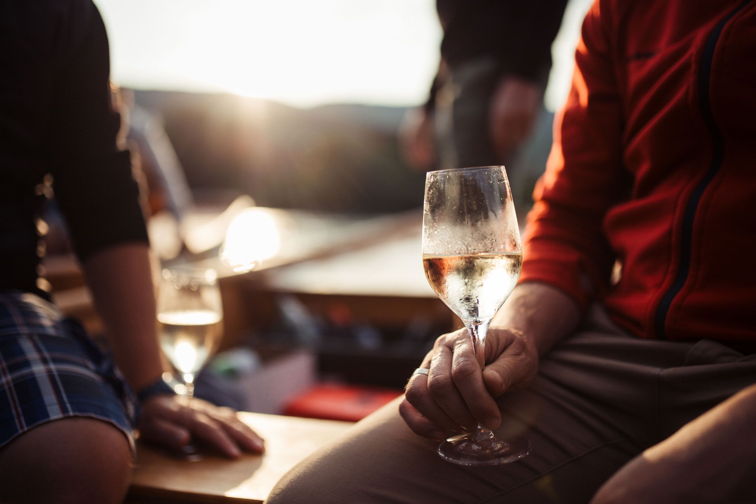 Borospoharat tartó személy, a háttérben naplemente.