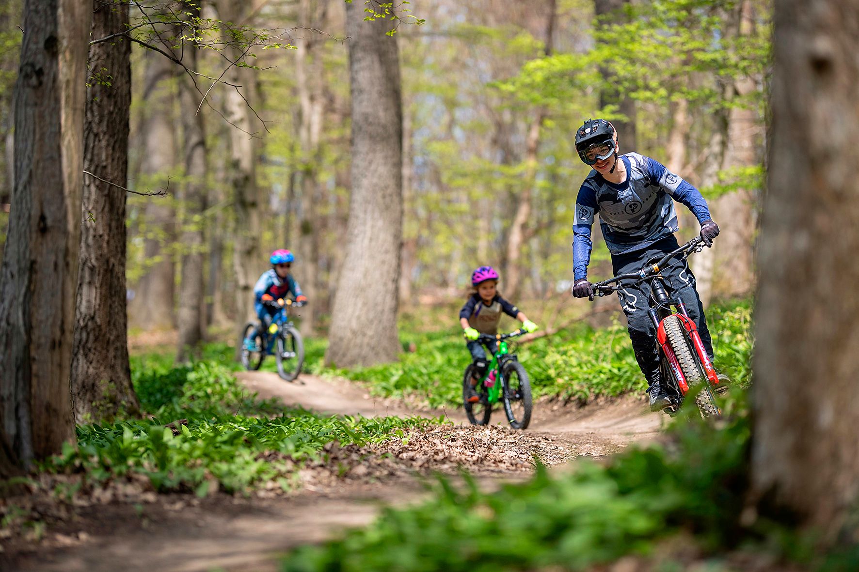 Három hegyikerékpáros teker egy erdei ösvényen.