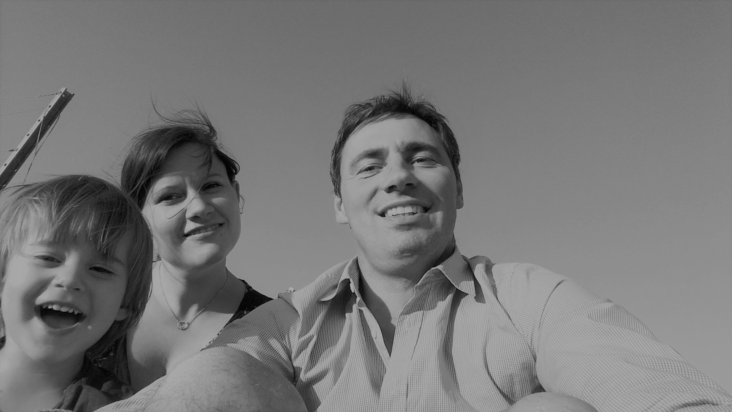 Fekete-fehér fotó egy mosolygó családról, amely egy férfiból, egy nőből és egy gyermekből áll, és a kamerába néz.
