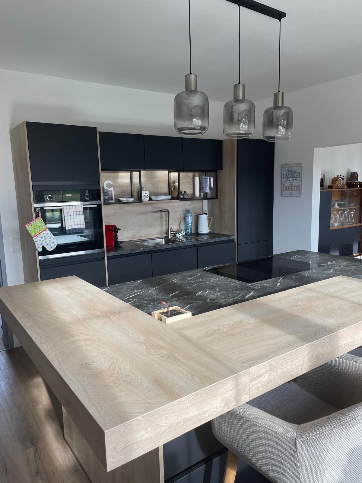 Modern konyha fa és márvány elemekkel, három függőlámpával és fekete szekrényekkel.