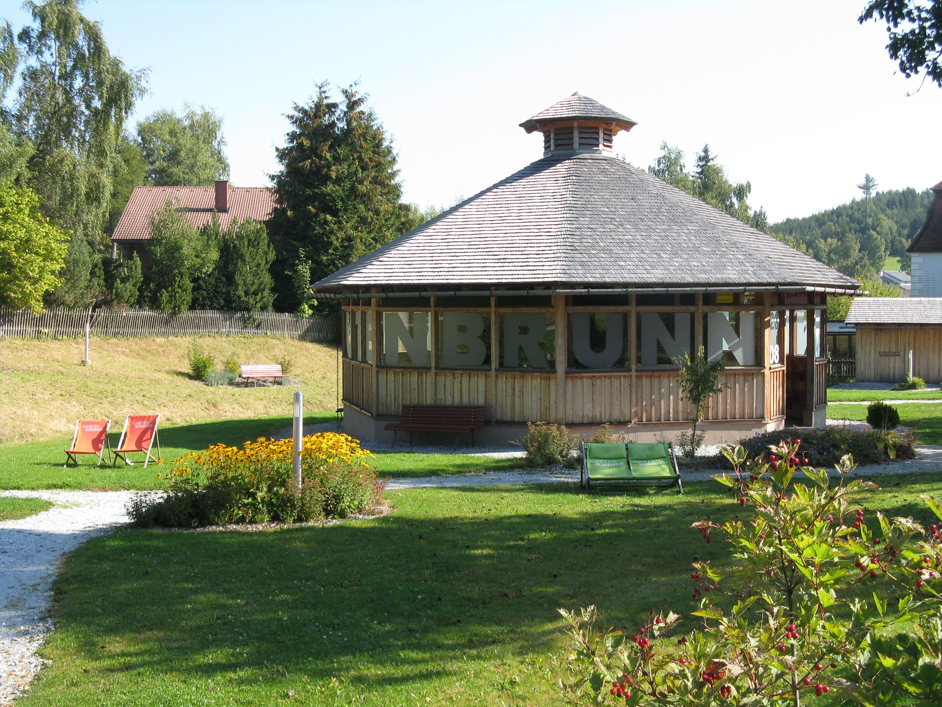 Pavilon egy zöld parkban, virágokkal és nyugágyakkal.