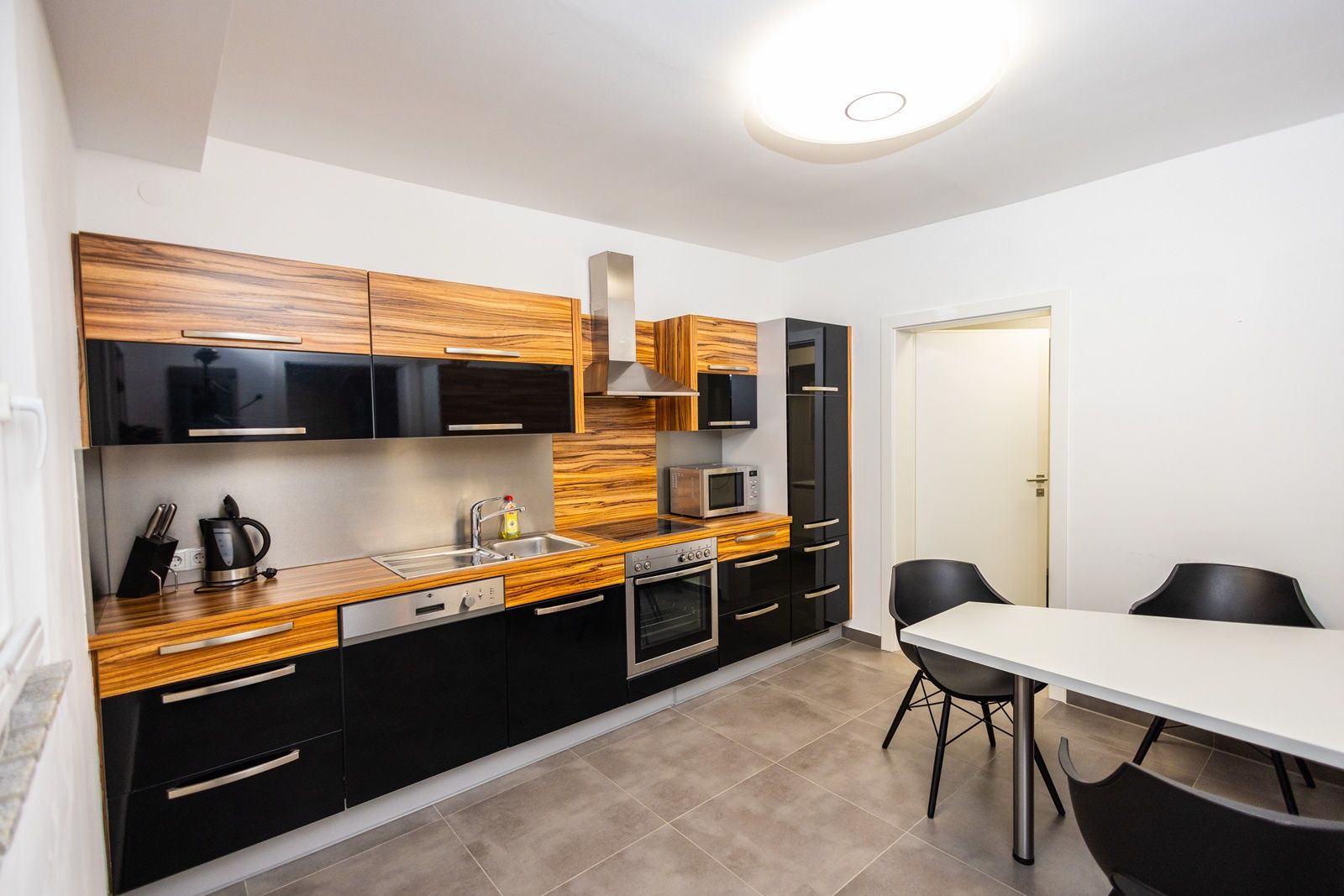 Modern konyha fából készült és fekete, magasfényű frontokkal, étkezőasztallal és székekkel.