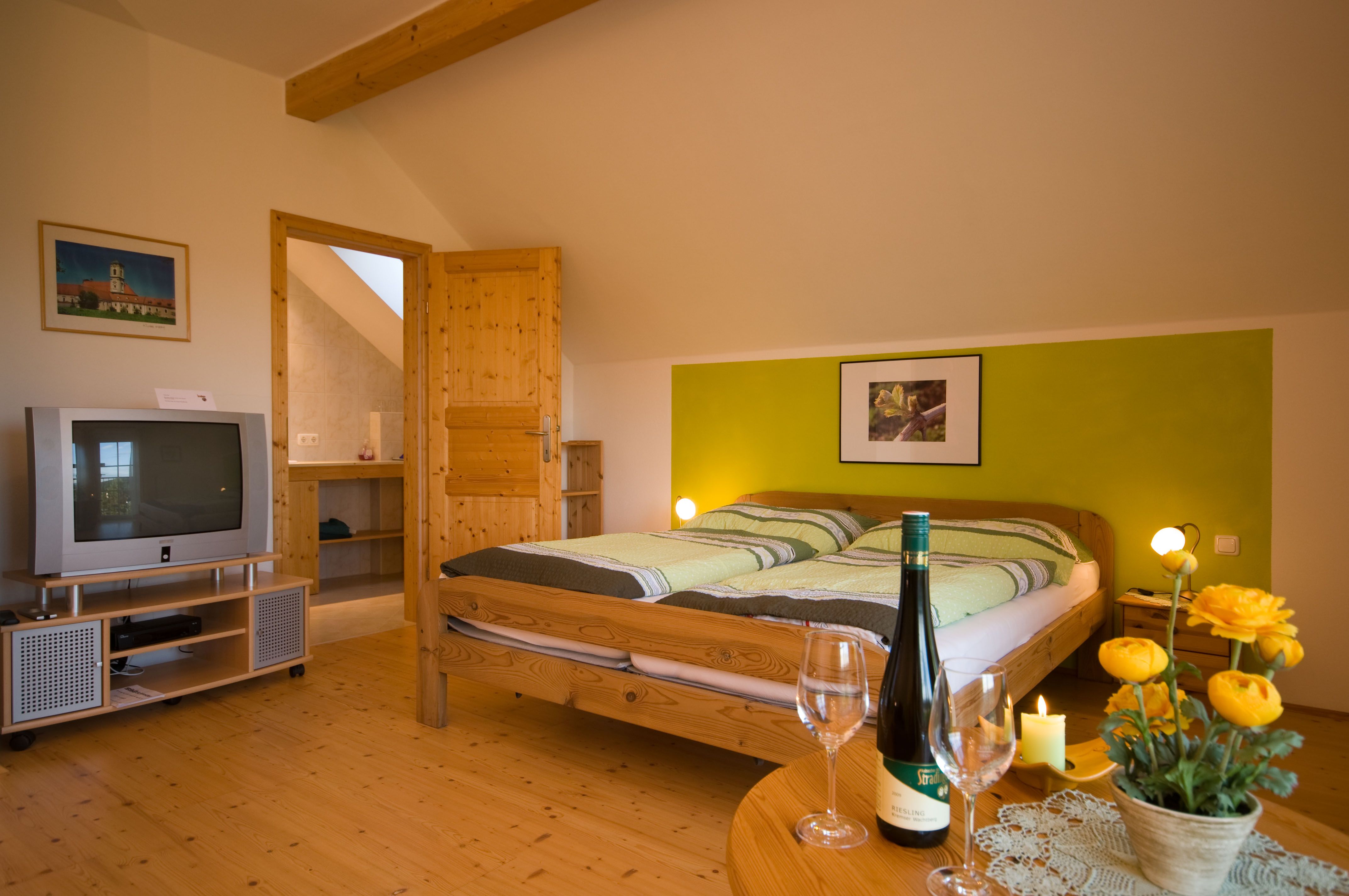 Hangulatos szoba franciaággyal, TV-vel, egy üveg borral és virágokkal az asztalon.