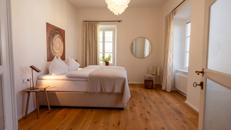 Hangulatos h&aacute;l&oacute;szoba francia&aacute;ggyal, fapadl&oacute;val, falik&eacute;pekkel, kerek t&uuml;k&ouml;rrel &eacute;s n&ouml;v&eacute;nyekkel az ablakp&aacute;rk&aacute;nyon.