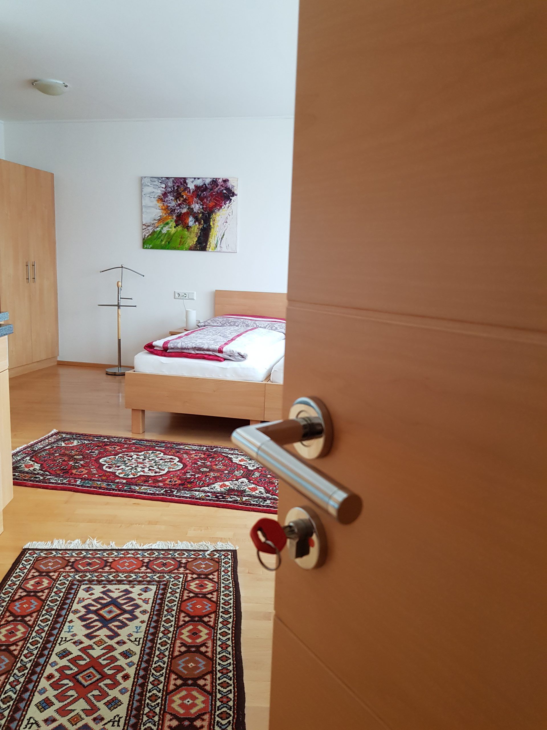 Egy nyitott terű szoba egy ággyal, szőnyegekkel és egy festménnyel a falon.