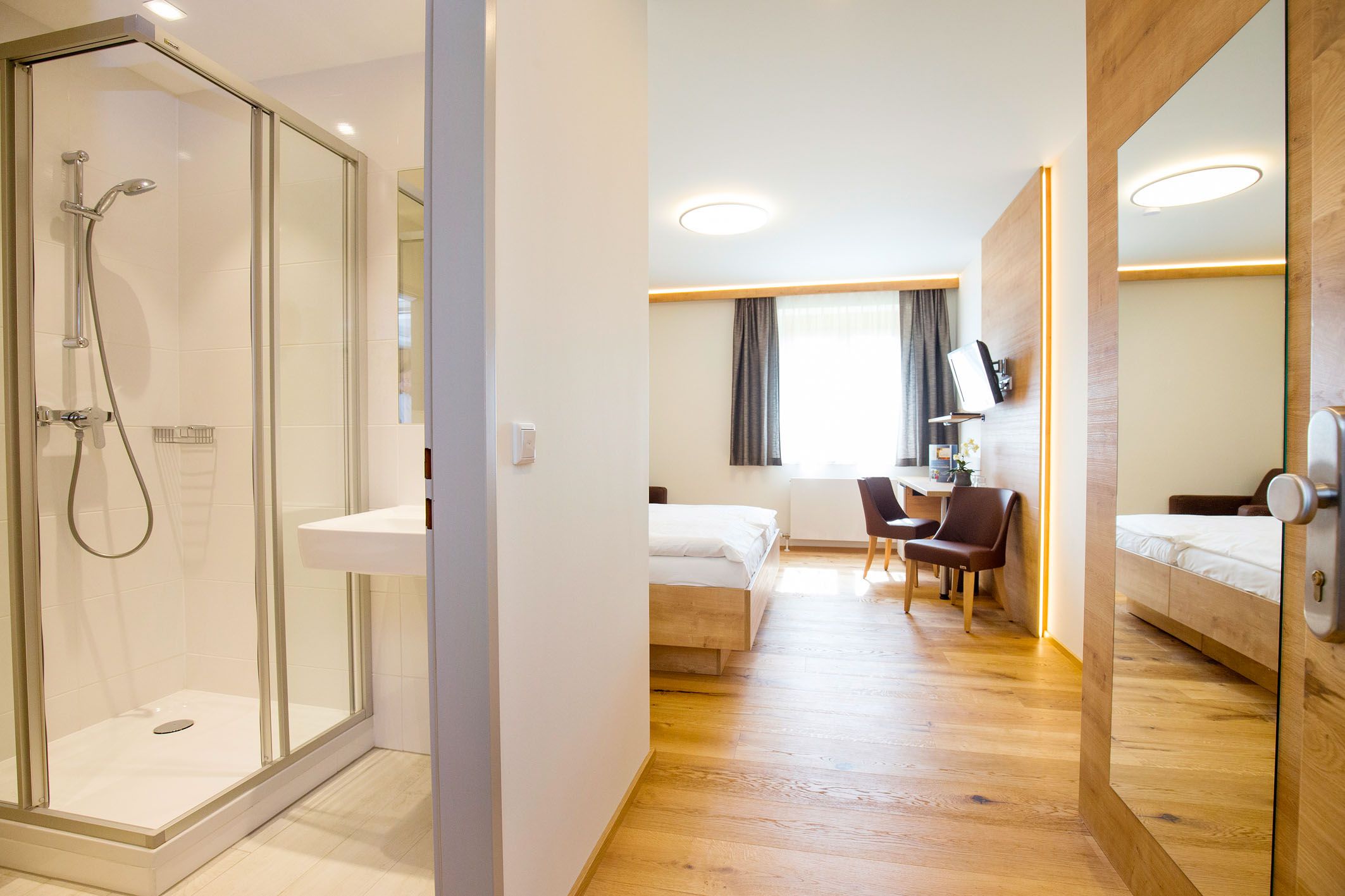 Modern szállodai szoba fürdőszobával, ággyal, íróasztallal és székekkel.