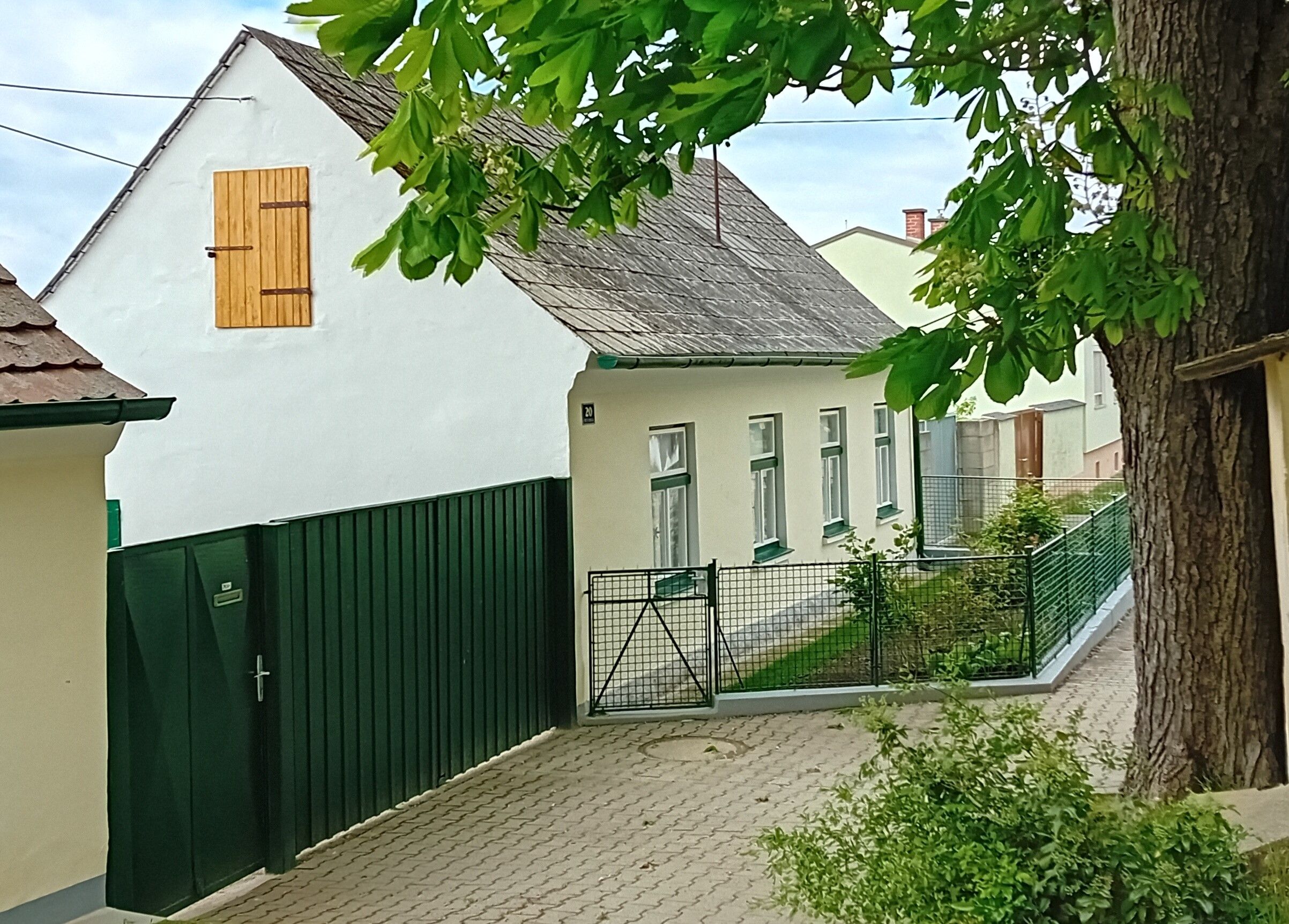 Hagyományos fehér nyaralóház zöld kerítéssel és fával az előtérben.