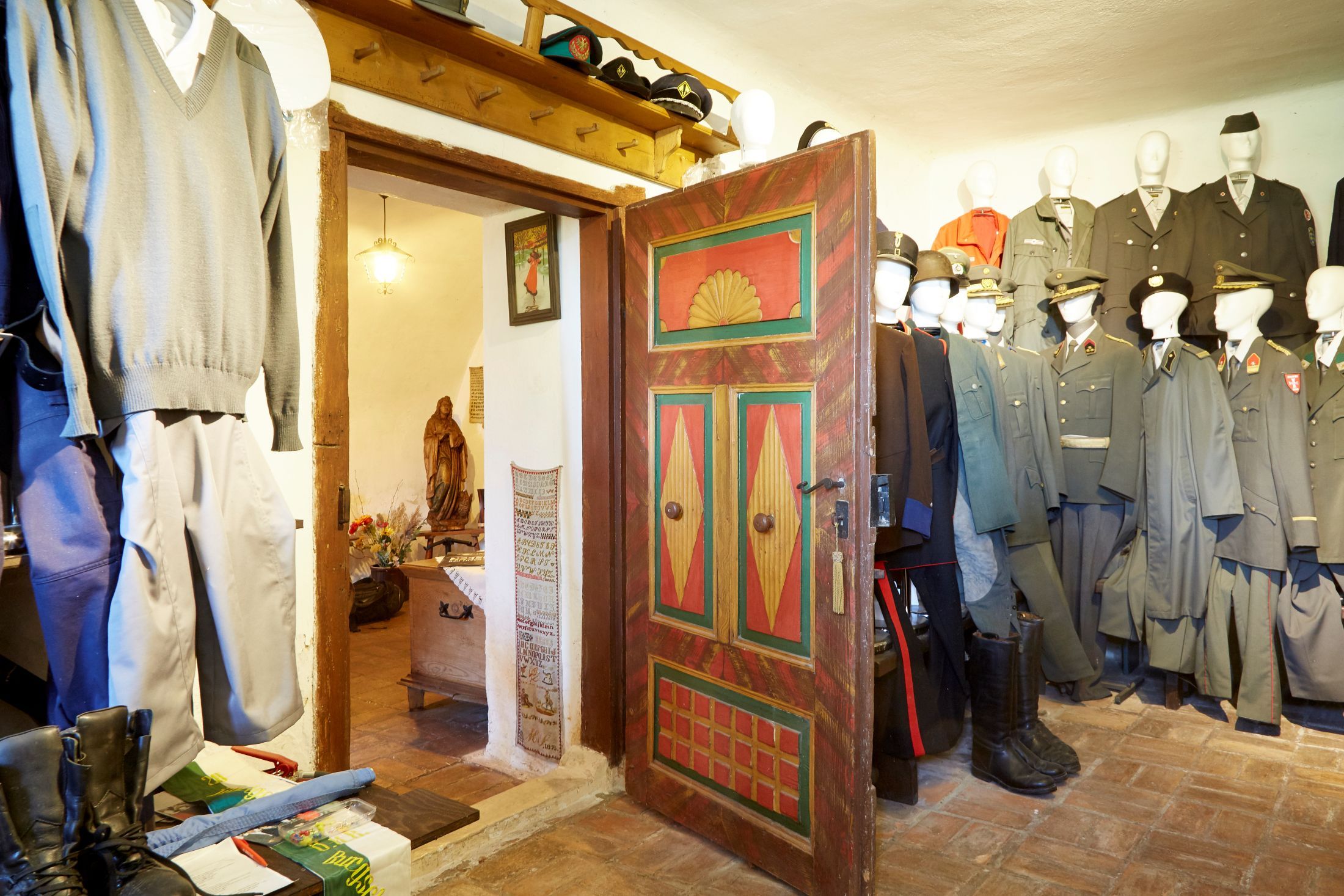 Egy szoba belső nézete régi egyenruhákkal és egy színesre festett faajtóval.