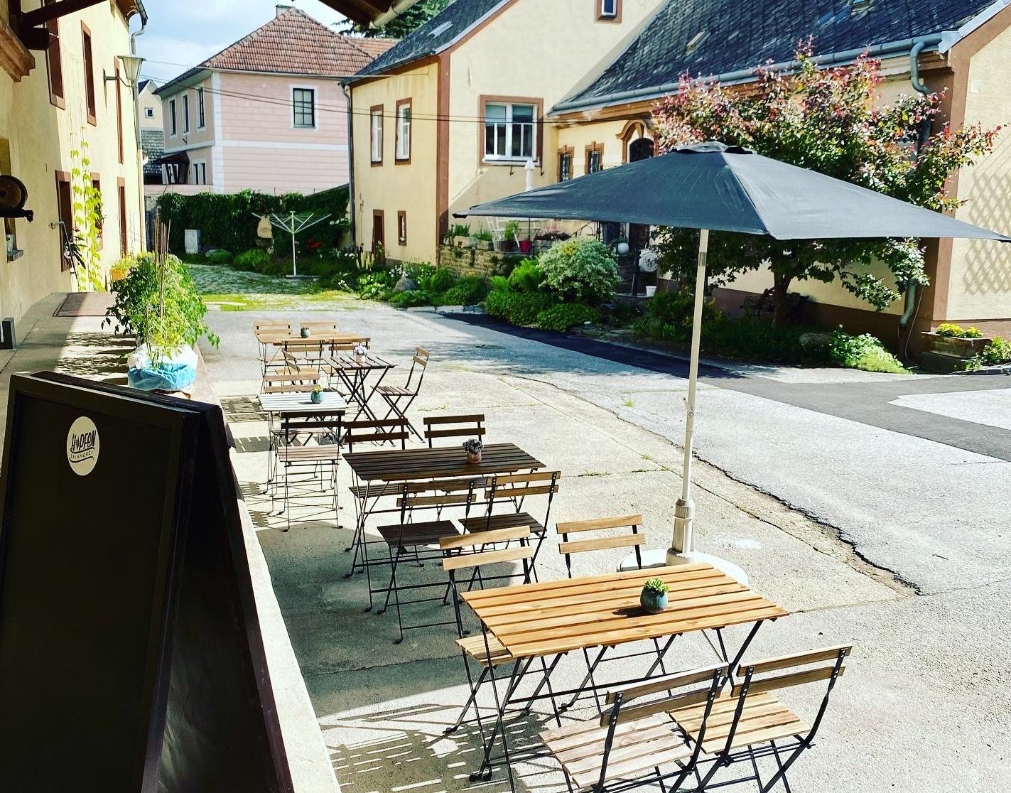 A belső udvaron fából készült asztalokkal és székekkel, napernyővel és növényekkel berendezett vendégkert.